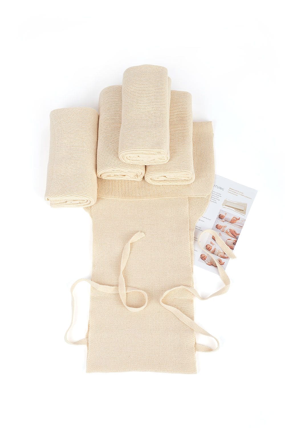 aufgerollte Finkhof Strickwindeln auf liegender Strickwindel mit Anleitung daneben, naturbelassen auf Bio Baumwolle