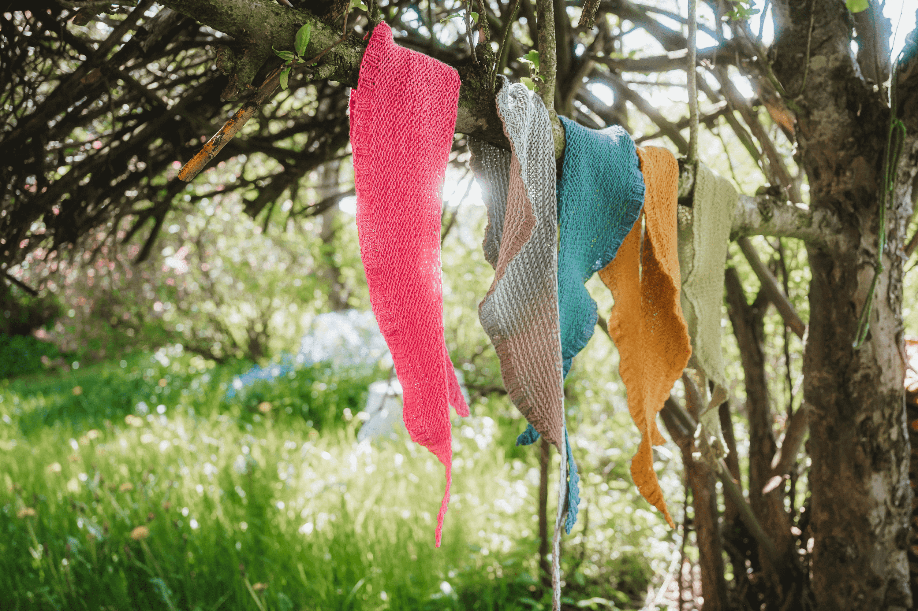 Gestrickte Schals aus Finkhof Wolle in Mondsichelform hängen in verschiedenen Farben über einem Ast