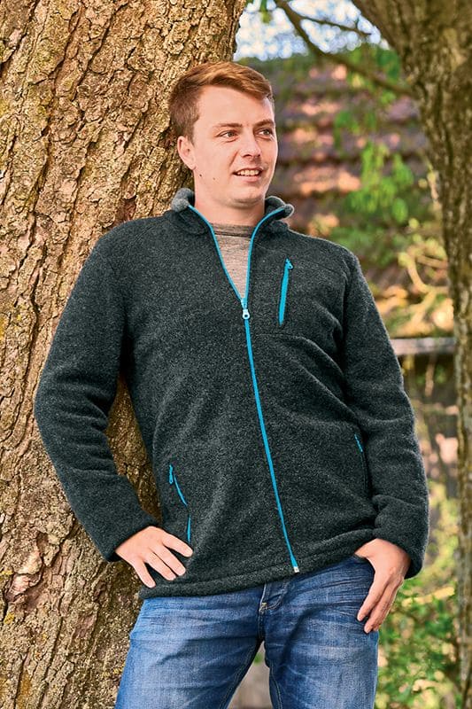 Mann lehnt an Baum und trägt anthrazitfarbene Wollflecejacke aus bio Wolle (kbT) mit türkisen Reißverschlüssen und Stehkragen
