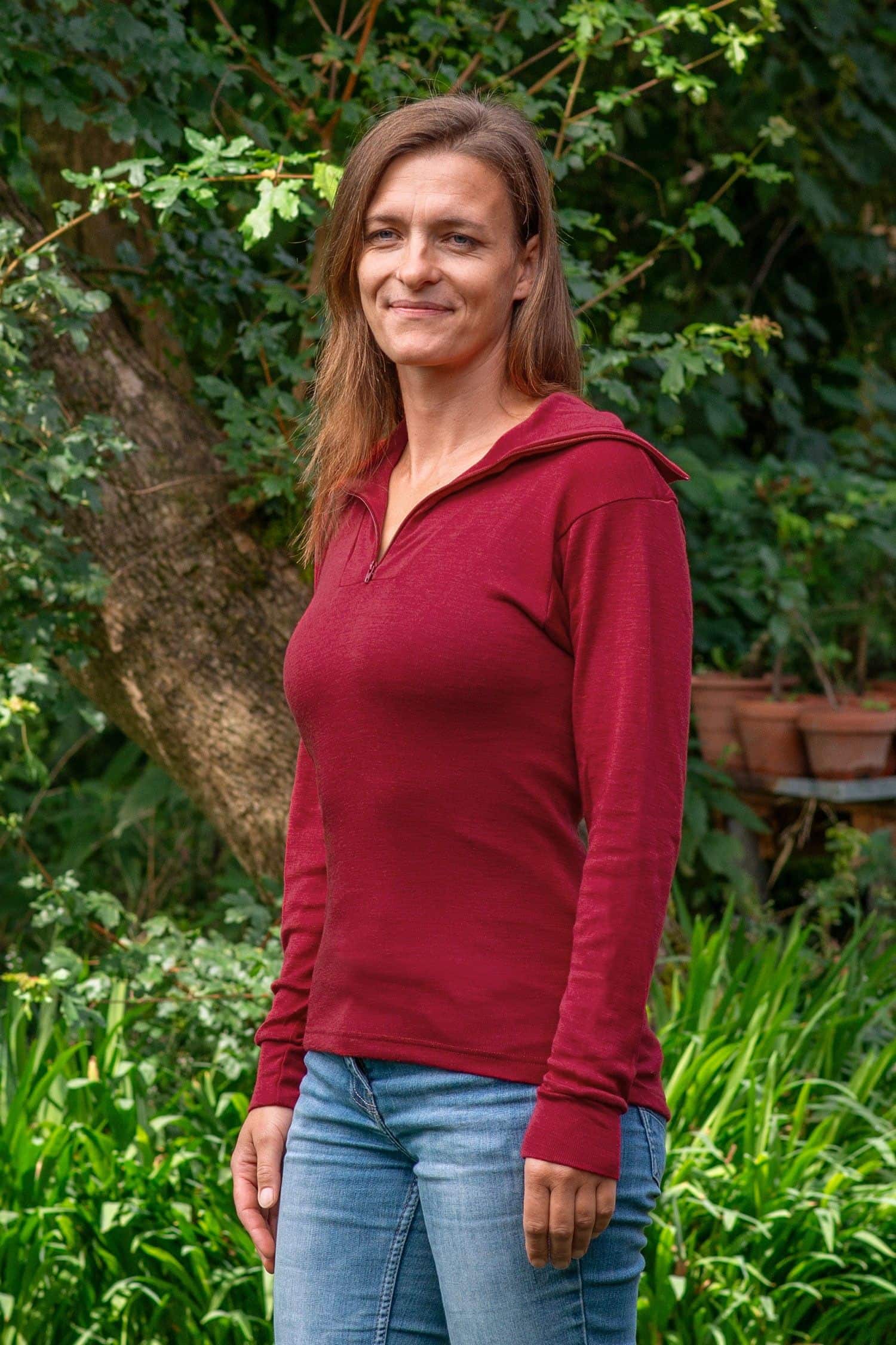Frau steht im Garten und trägt Jeans und roten Sportrolli aus bio Wolle (kbT) und Seide mit Reißverschluss
