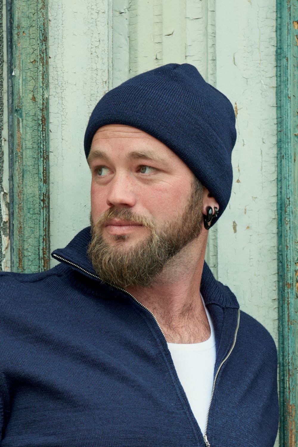 Mann trägt dunkelblauen Pullover mit Zipper und marineblaue leichte Mütze aus bio Wolle (kbT) und bio Baumwolle (kbA)