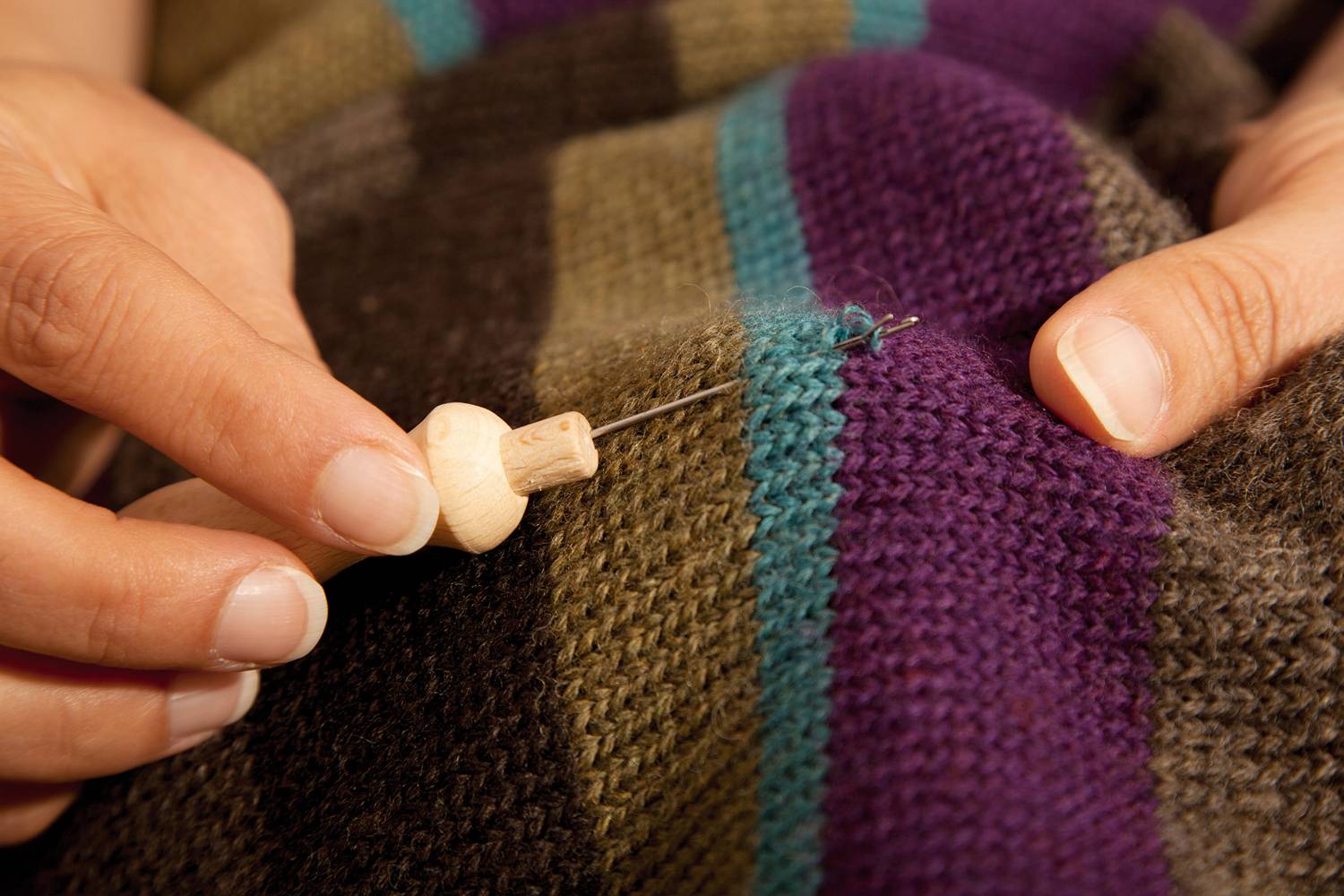 Hand zieht mit Finkhof Einziehnadel Faden in gestreiften Wollpullover