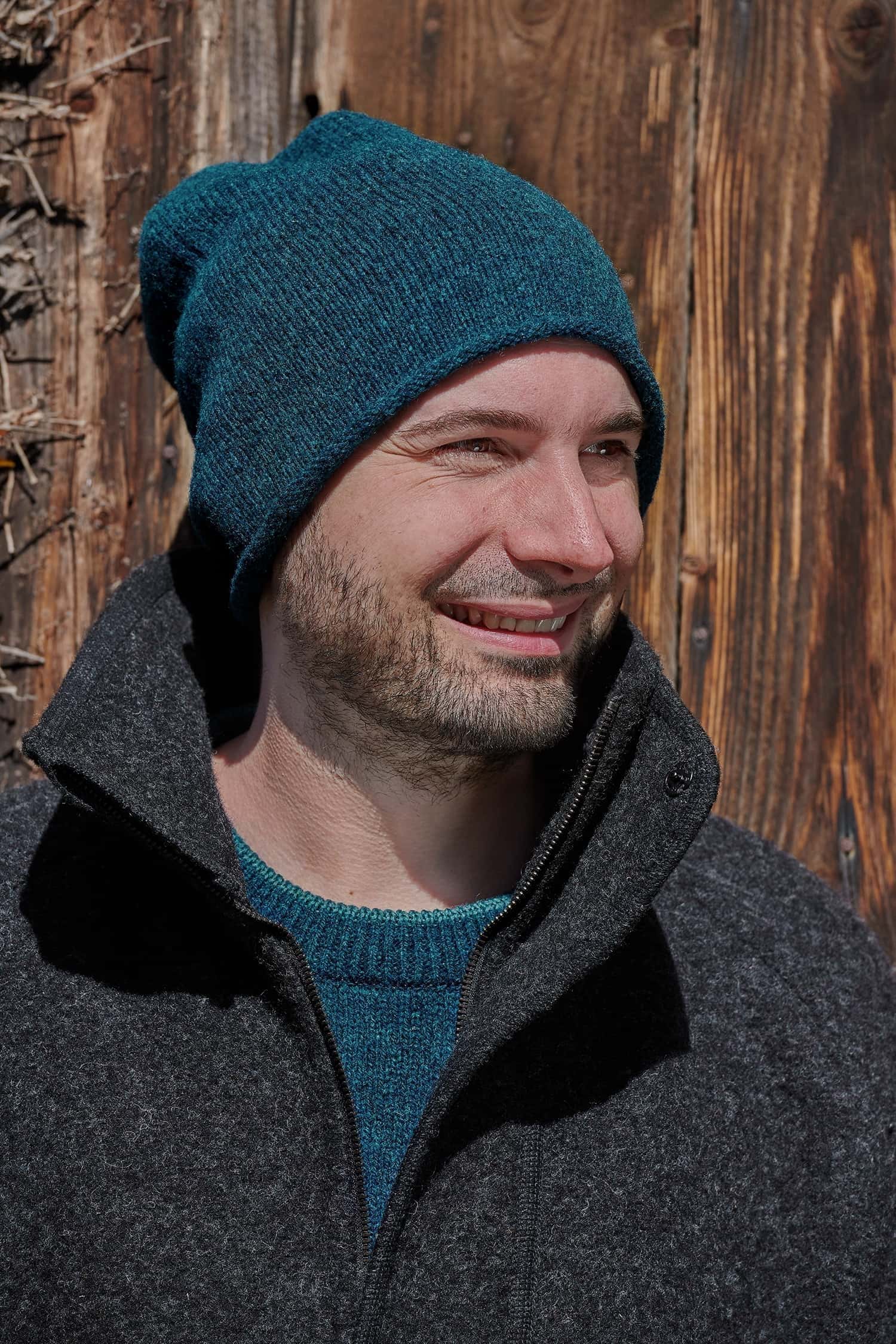 Mann trägt eine seeblaue Strickmütze aus Bio-Wolle vom Finkhof mit einem türkisen Pulli und einer schwarzen Jacke