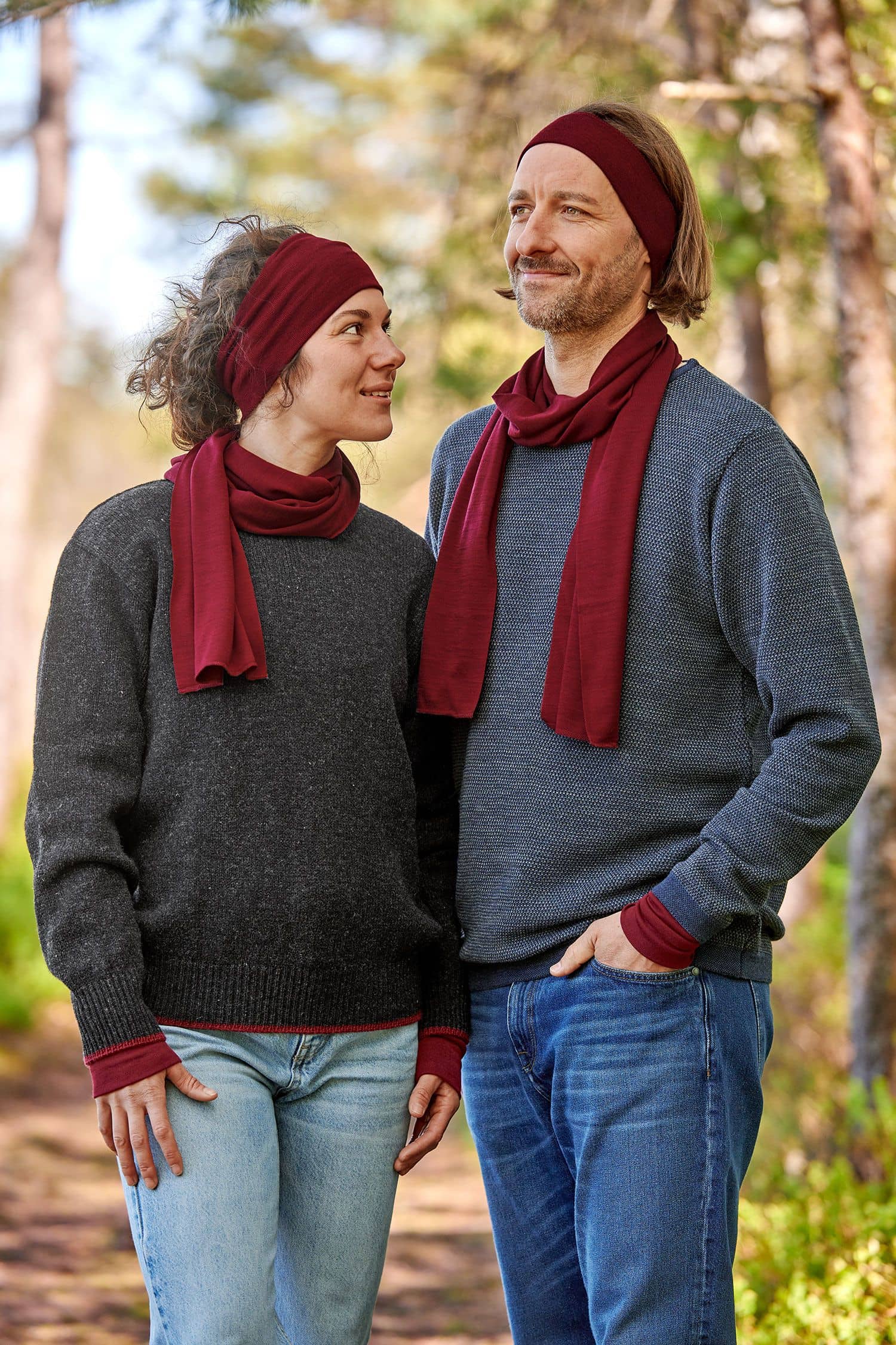 Mann und Frau mit dunklen Pullis tragen bordeauxrote Stirnbänder, Schals und Pulswärmer aus bio Wolle (kbT) und Seide