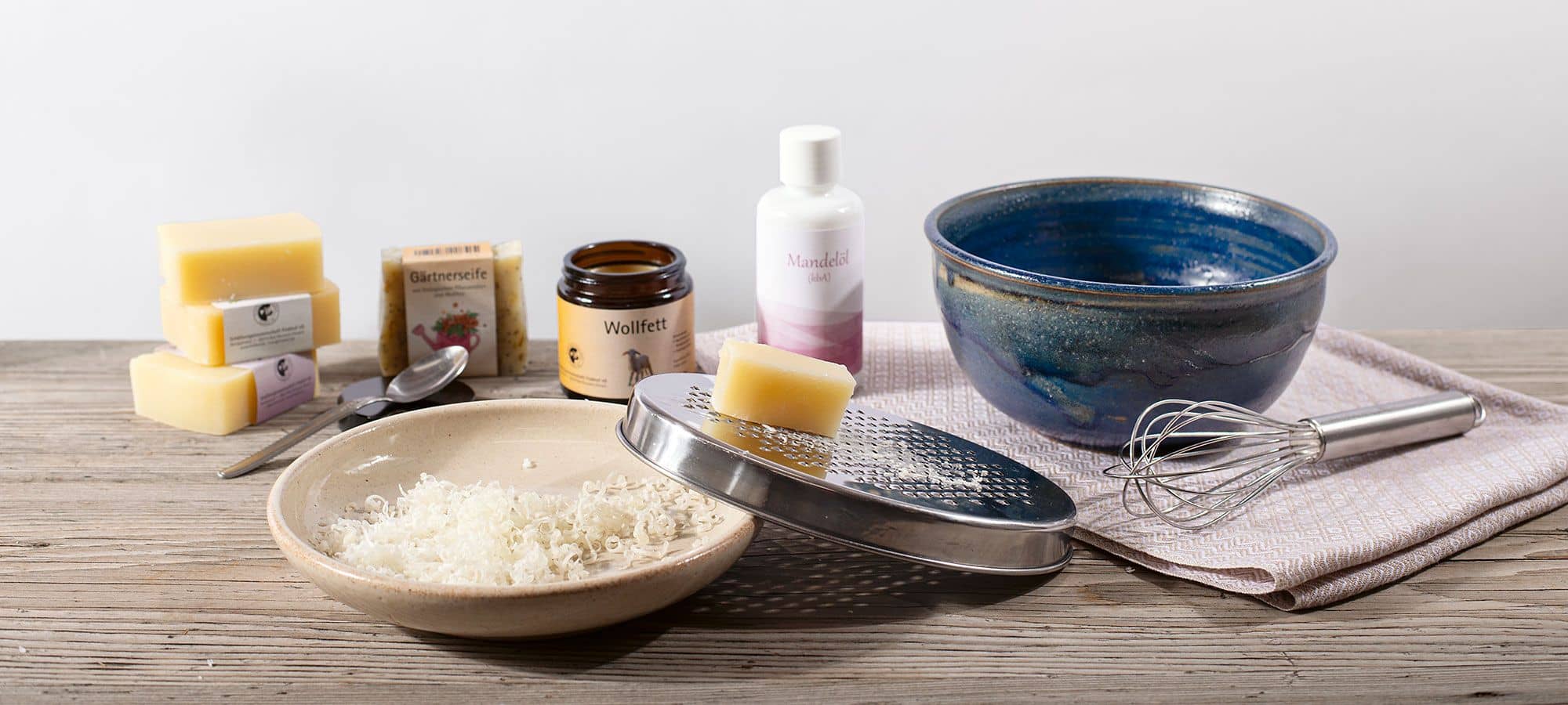 Zutaten für selbstgemachte Duschcreme auf Holztisch mit Schüsseln, Reibe für Seife und Schneebesen