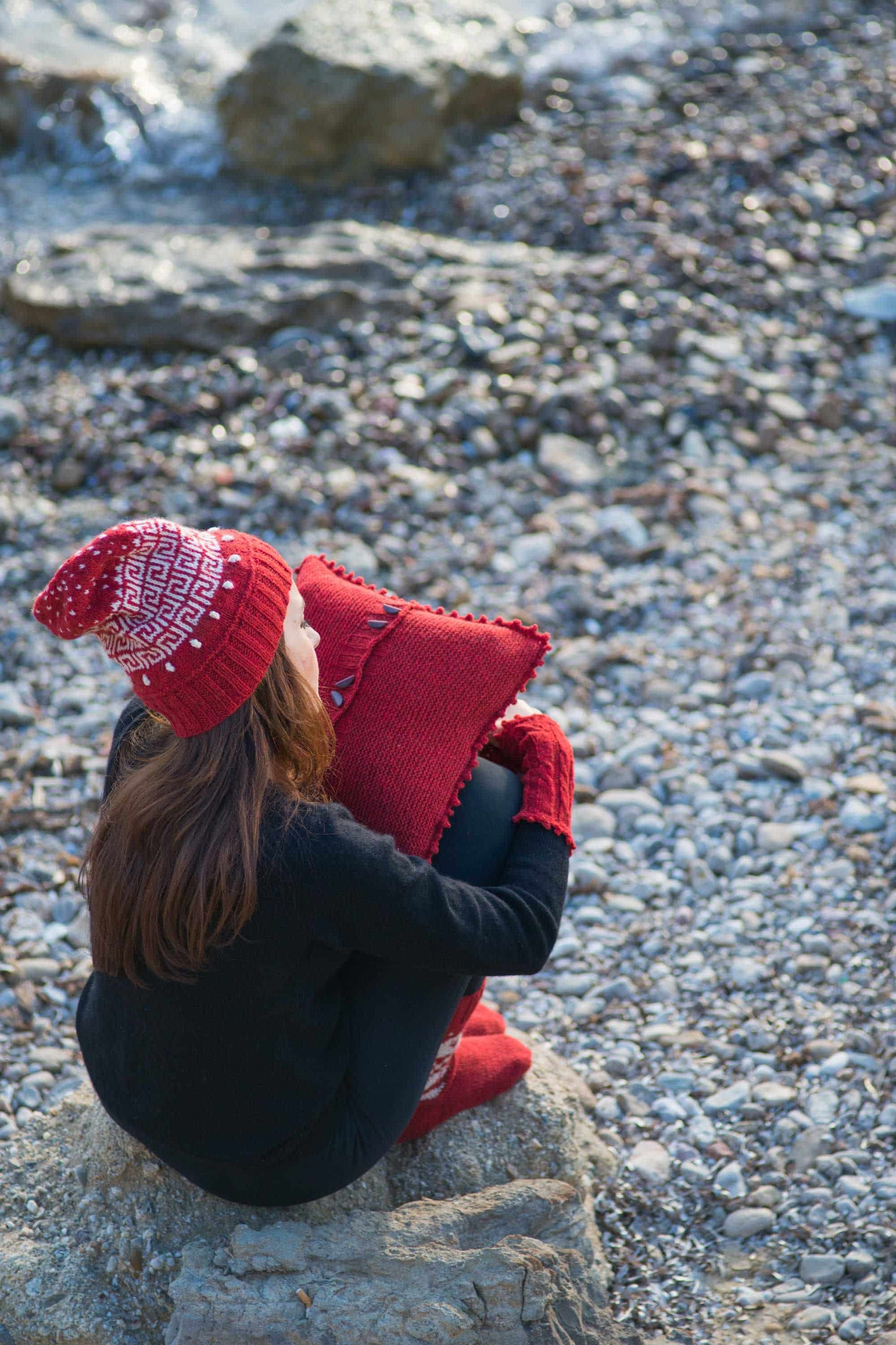 rote Mütze mit Muster, rotes Kissen und Pulswärmer als Beispielprojekte für das Buch ,,Ariadnes Fäden", Steinhintergrund