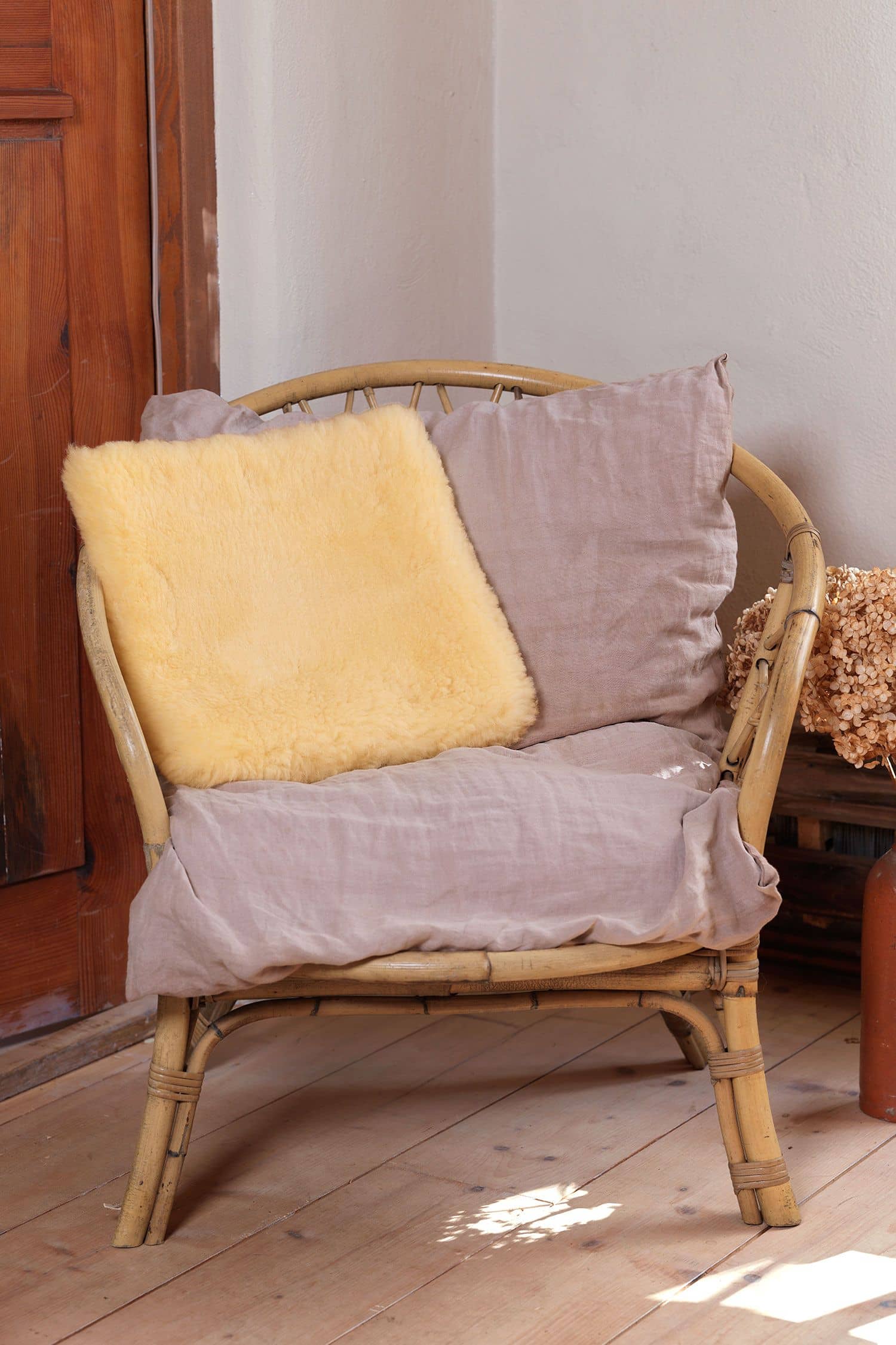 quadratisches Wohlfühlkissen aus relugan gegerbtem Finkhof Fell liegt auf einem Korbstuhl