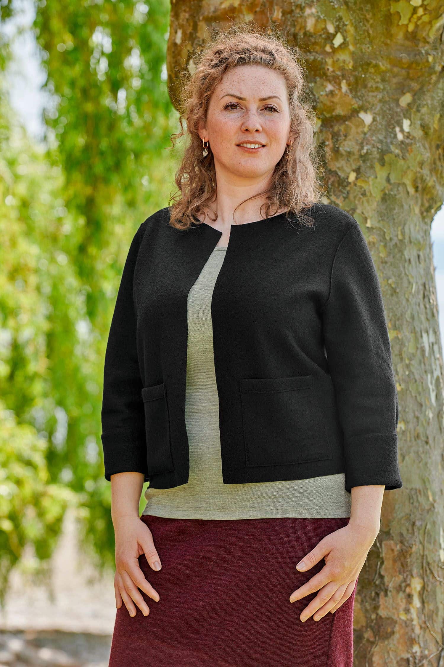 Frau mit rotem Rock und grünem Shirt trägt eine schwarze Feinstrick Kurzjacke aus bio Wolle (kbT) vom Finkhof