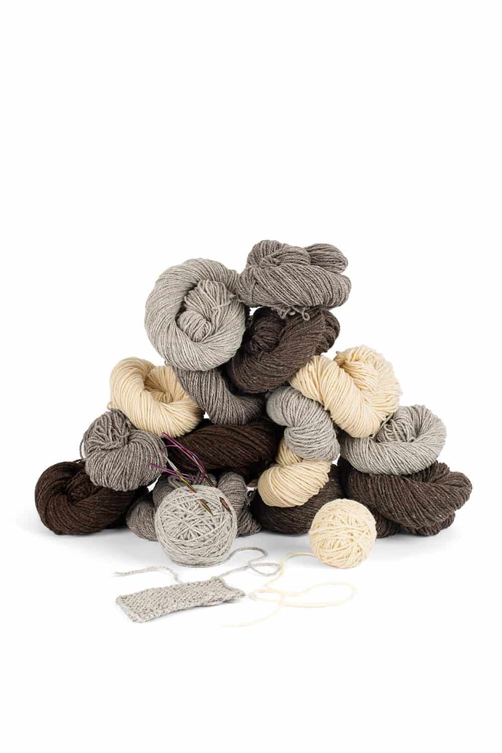 Finkhof Merinowolle dick ungefärbt Dicke, ungefärbte bio Merinowolle (kbT) vom Finkhof, aufgestapelt mit Strickstück, Knäueln und Stricknadeln davor