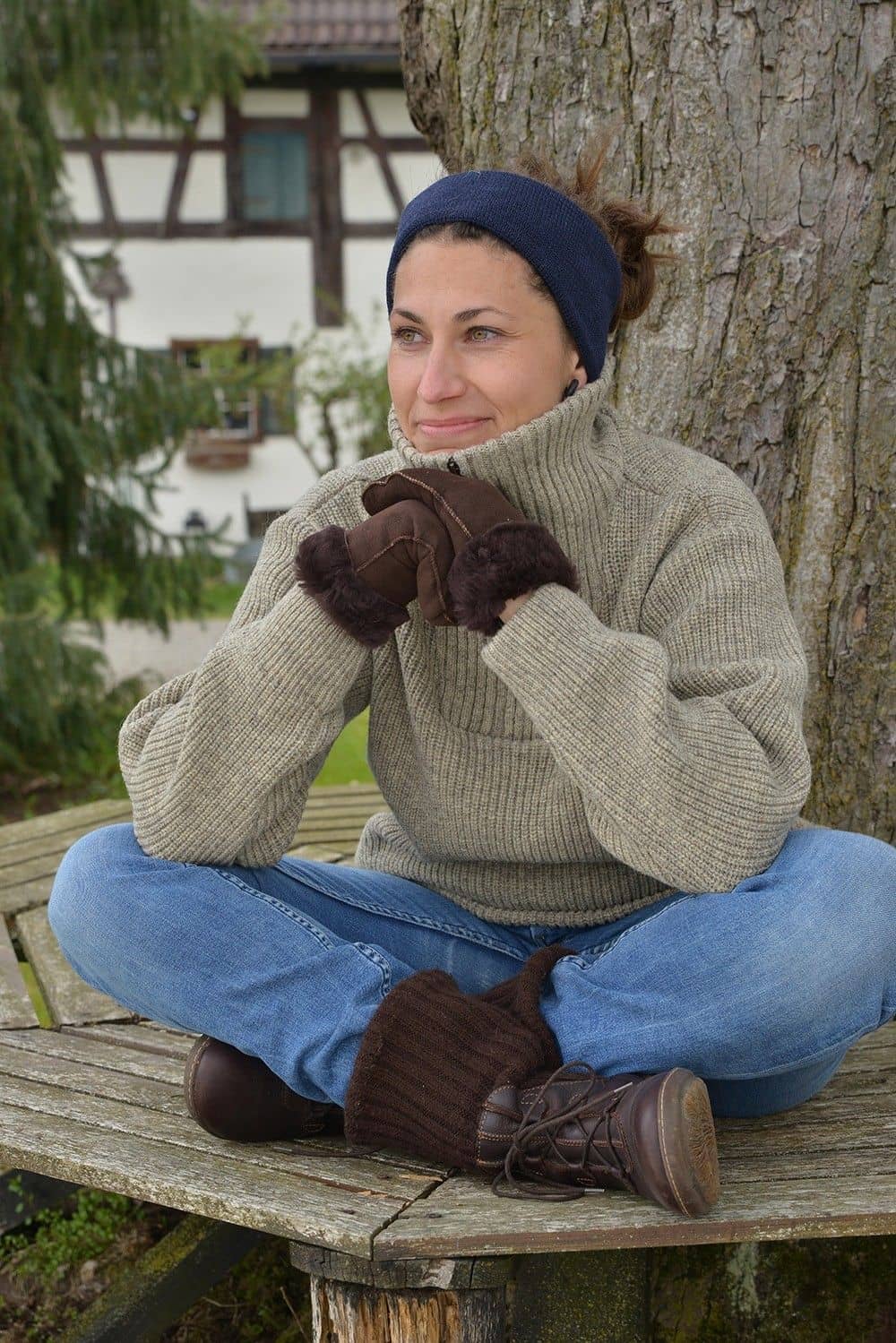 Frau sitzt auf Bank und trägt dunkelbraune Fell- Fausthandschuhe aus Pelzvelour ohne Bund und grauen Pulli