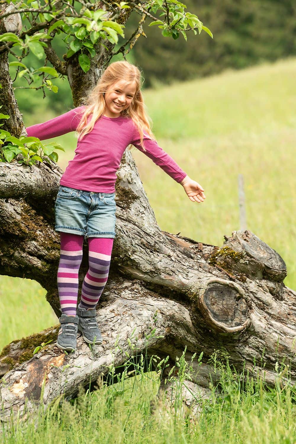 Kind balanciert auf Baumstamm und trägt fuchsiafarbenes Wolle Seide Langarmshirt aus bio Wolle (kbT)