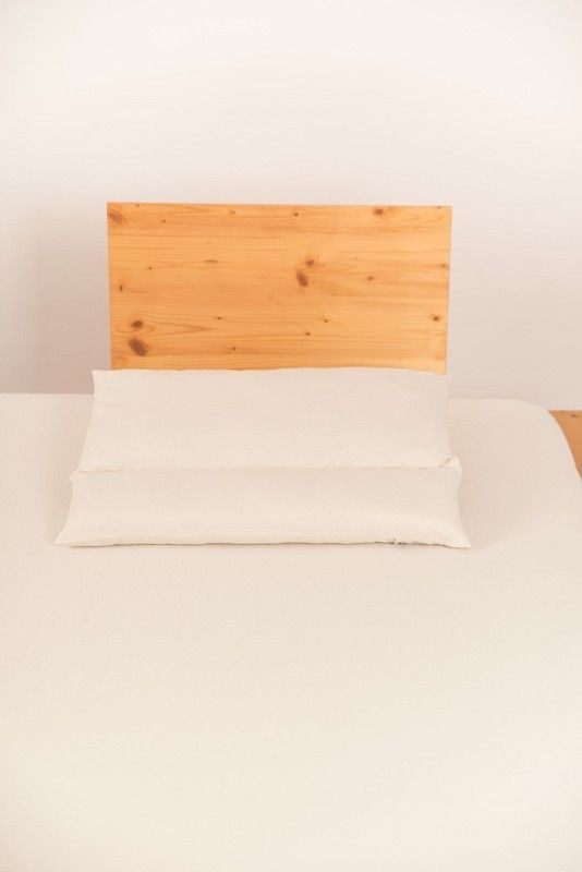weißes Rollenkissen in 40x60cm aus bio Wolle (kbT) und bio Baumwolle (kbA) vom Finkhof auf hellbraunem Bett