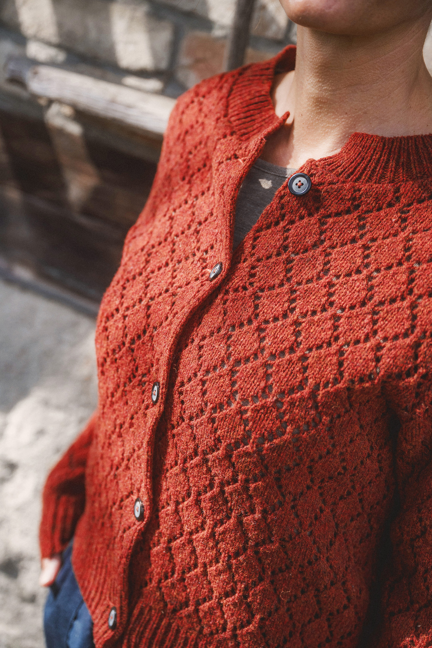 Frau trägt eine weite Hose und ein braunes Shirt mit einer rot orangen Strickjacke mit Ajourmuster aus Bio-Wolle vom Finkhof