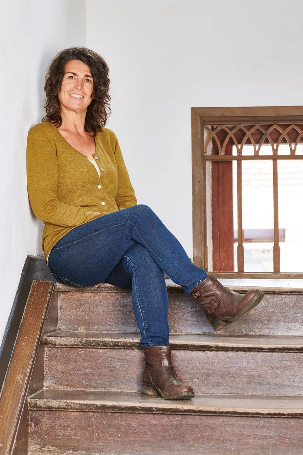 Frau sitzt auf Treppe und trägt gelbmelierten Cardigan aus bio Wolle (kbT) und Jeans