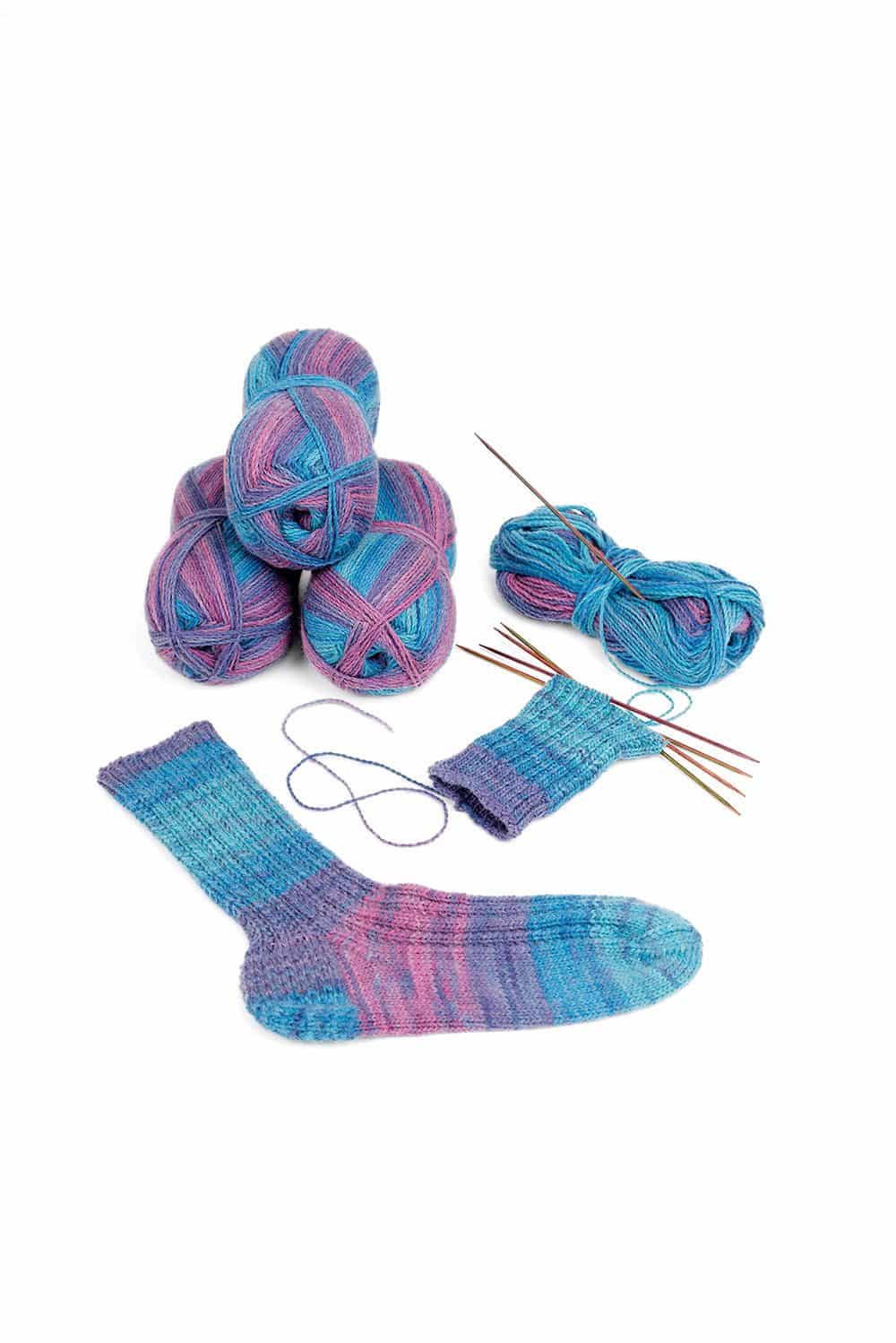feine Finkhof Sockenwolle mit blau lila Farbverlauf aus bio Wolle (kbT) mit Knäulen, fertiger Socke und Stricknadeln