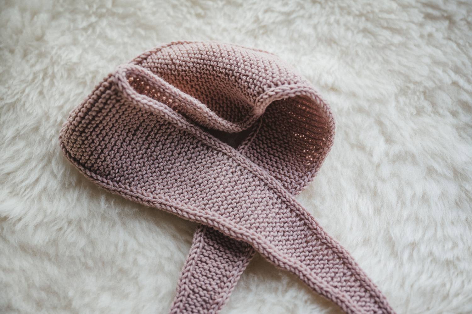 rosafarbener Mini-Schal aus der Finkhof Wolle Weich&Warm auf einem weißen Fell