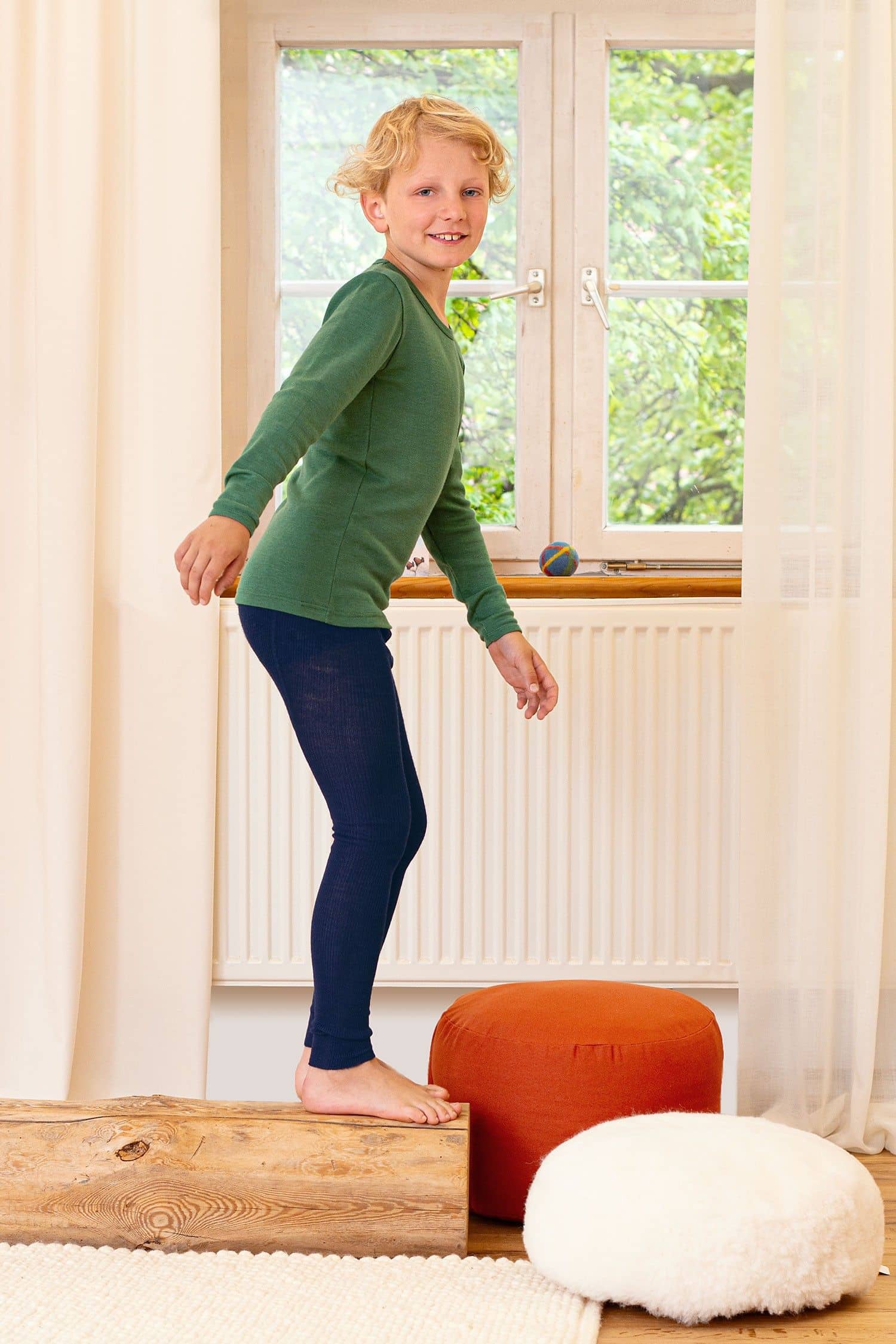 Kind steht auf Holzbalken und trägt eine marineblaue Leggings aus bio Wolle (kbT) und ein grünes Shirt