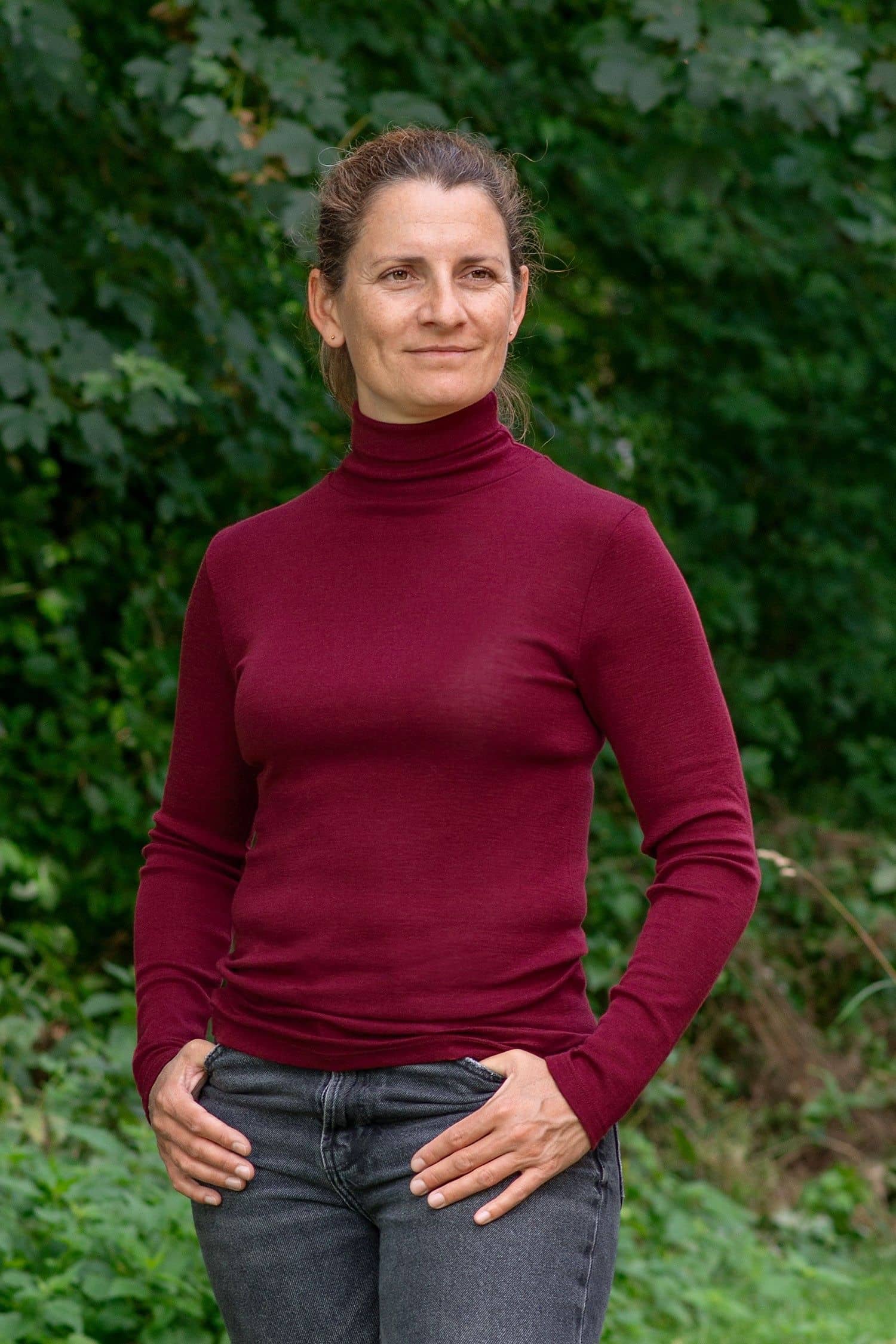 Frau im Garten trägt bordeauxrotes Langarmshirt mit Rollkragen aus bio Wolle (kbT) und Seide