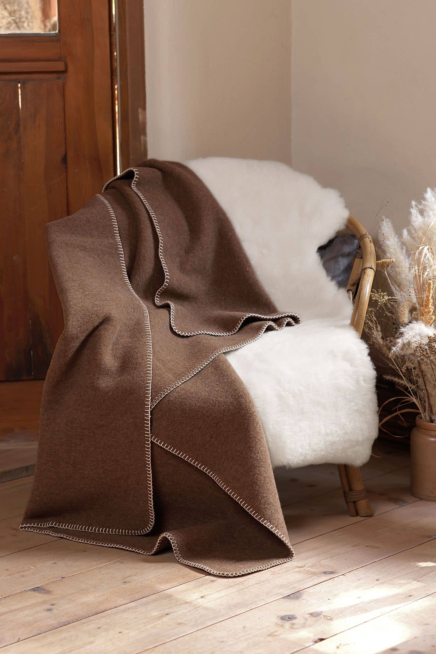 braune Wolldecke aus bioWolle (kbT) vom Juraschaf liegt auf Korbstuhl mit weißem Fell