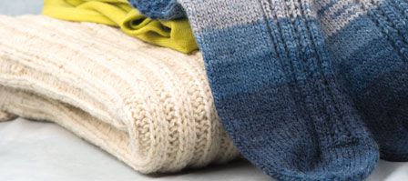 naturweißer Strickpulli auf dem blaue Stricksocken und weitere Kleidungsstücke liegen