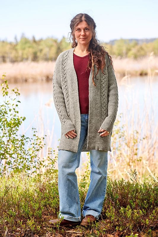 Finkhof-Zopfmuster-Cardigan ungefärbt Frau mit Jeans trägt ein rotes Shirt und einen grauen ungefärbten Cardigan mit Zopfmuster aus bio Wolle (kbT) vom Finkhof