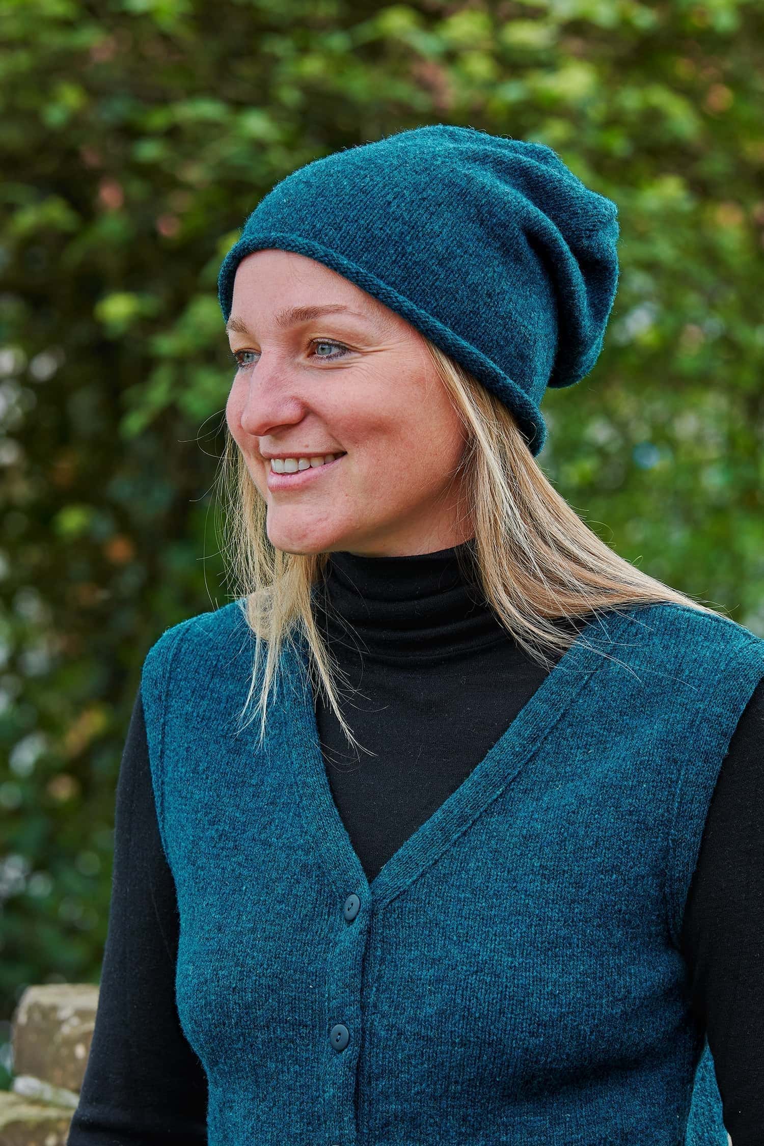 Frau trägt eine seeblaue Strickmütze mit Rollrand aus Bio-Wolle vom Finkhof mit passender Weste und einem schwarzen Shirt