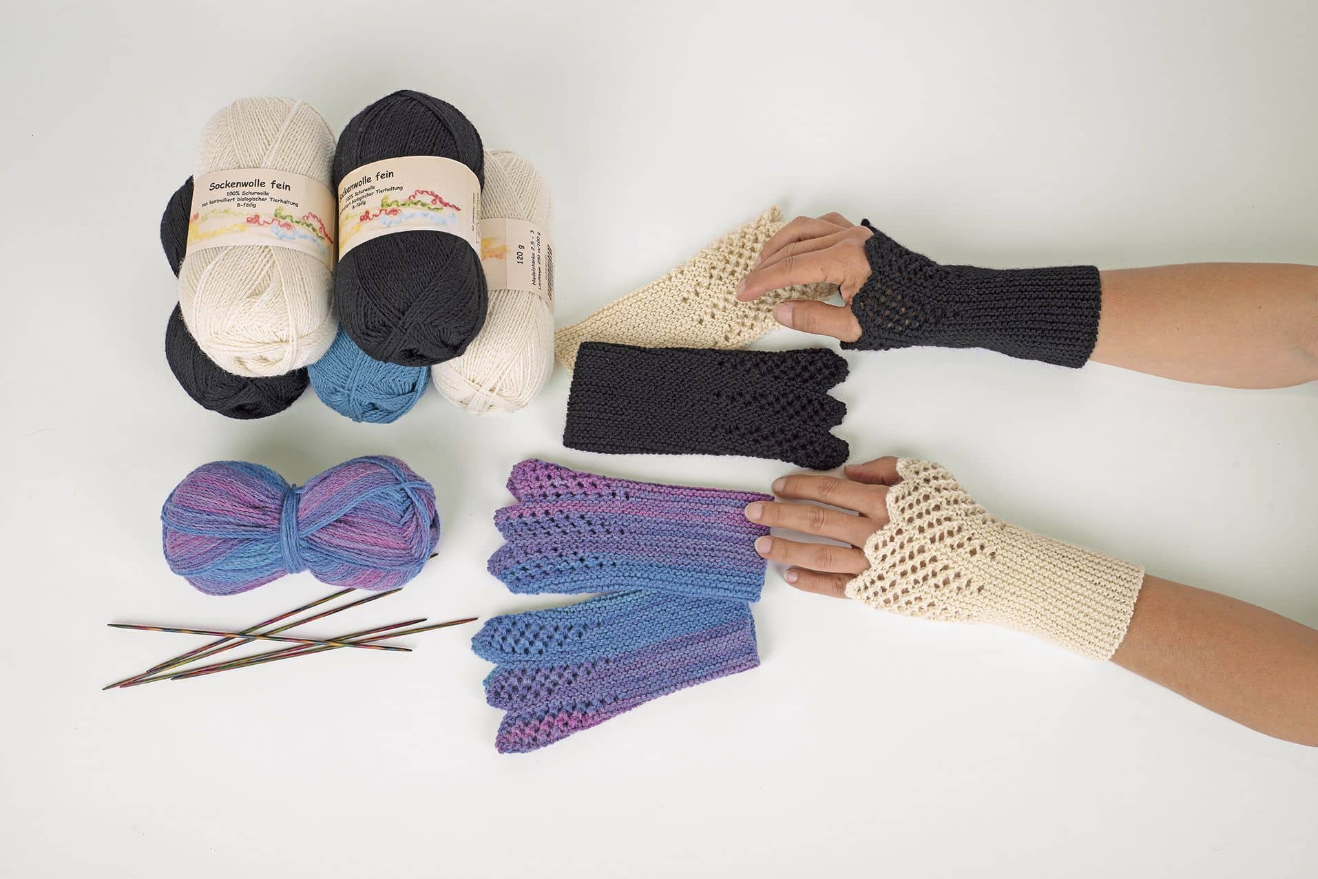 Frau trägt blaue und weiße Strickstulpen und blaue, weiße und lilane Wollknäule liegen daneben