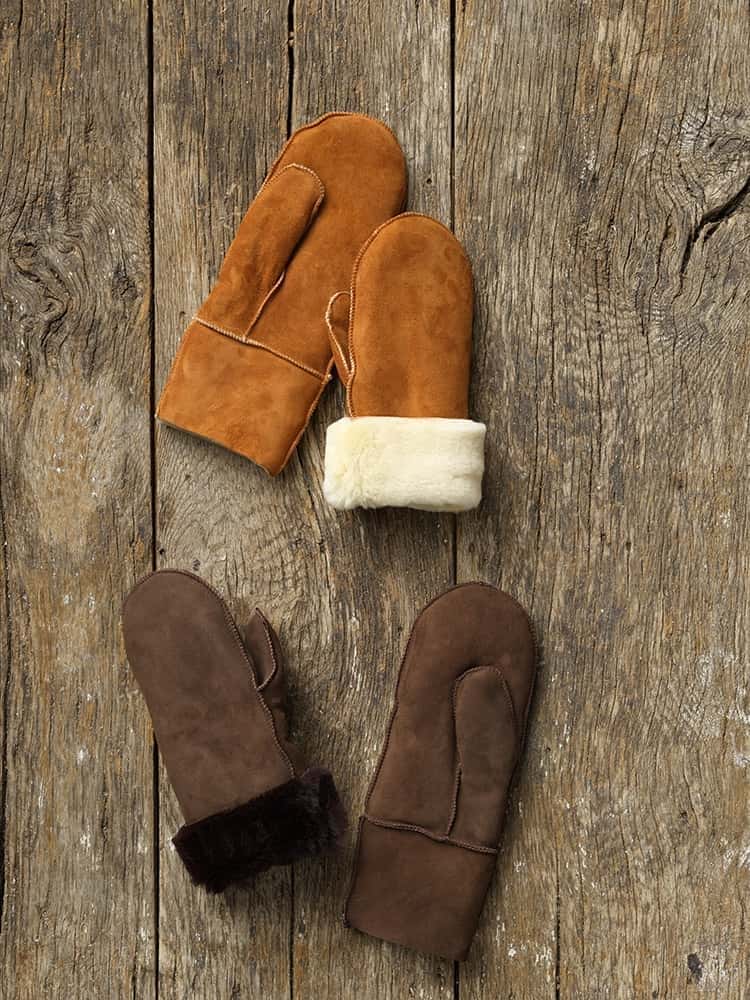 Fell-Fausthandschuhe ohne Bund Fausthandschuhe aus Fell ohne Bund in braun und hellbraun auf einem Holzboden