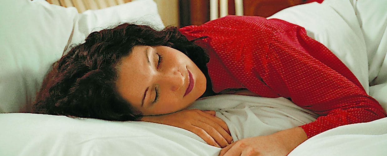 Frau mit rotem Schlafanzug und dunklen Haaren liegt auf Kissen mit weißem Bezug