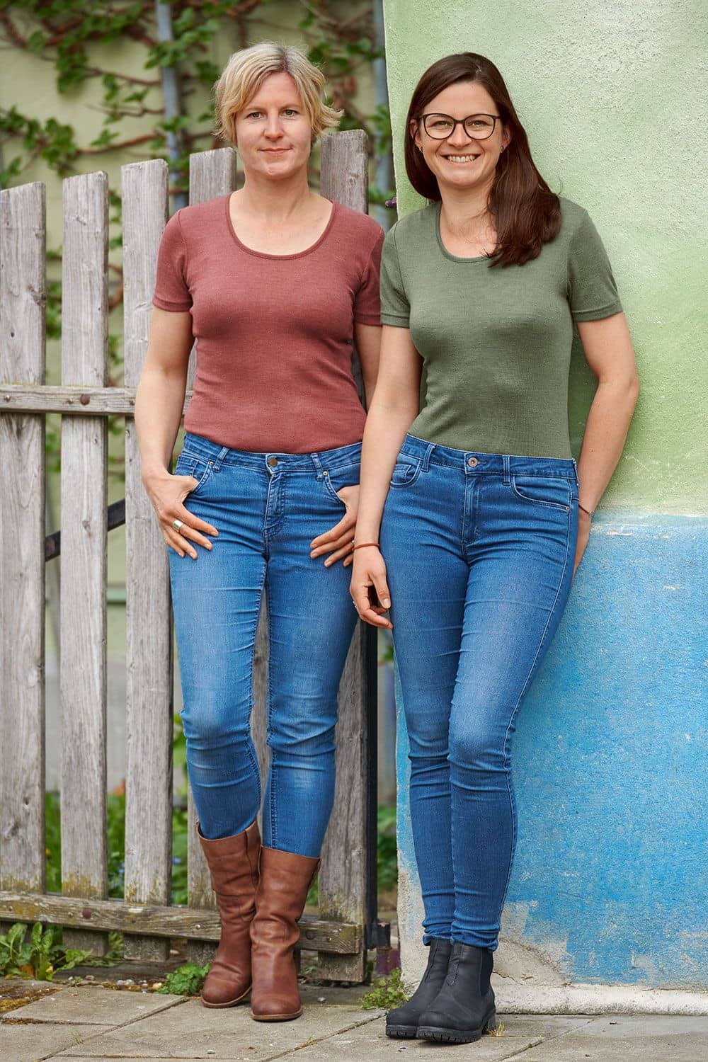 Wolle-Seide Damen T-Shirt Frauen tragen grünes und rotes kurzarm Shirt aus bio Wolle (kbT) und Seide mit Jeans, sie lehnen an einer Wand