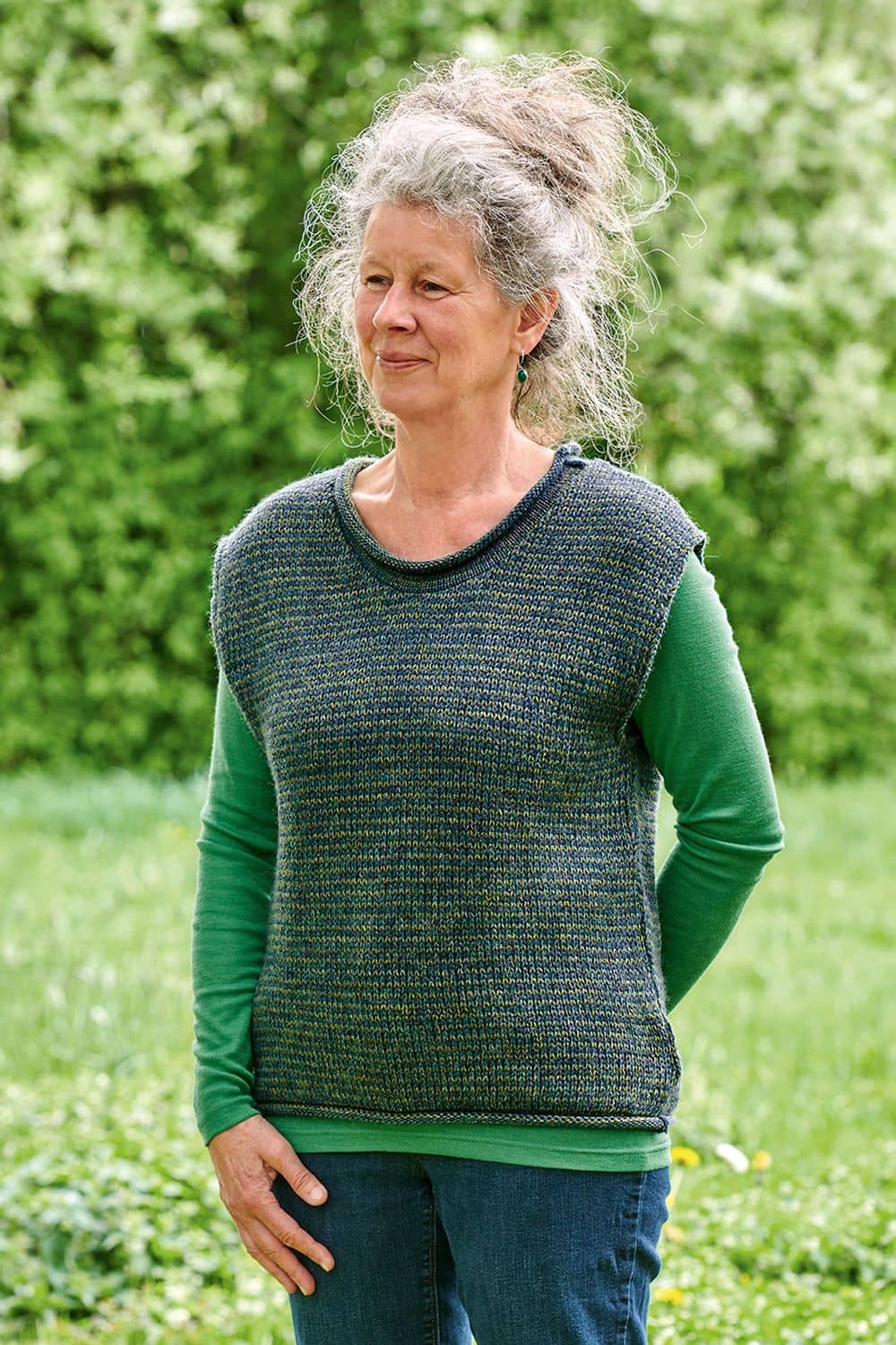 Frau auf Wiese mit grünem, Shirt trägt blau/grünmelierten Pullunder aus bio Wolle (kbT)