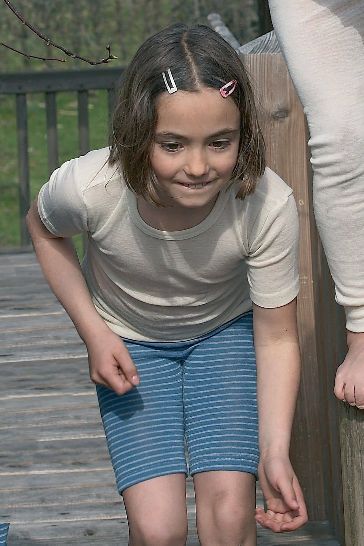 Mädchen trägt naturweißes kurzarm Wollunterhemd aus bio Wolle (kbT)mit blauer kurzer Ringelhose