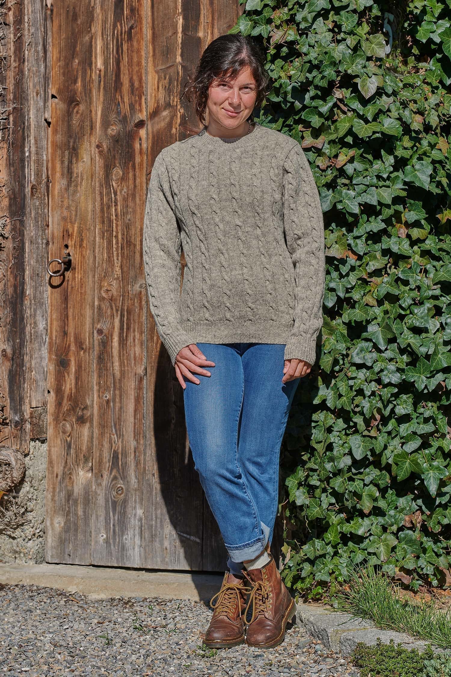 Frau trägt grauen Wollpullover vom Finkhof mit Zopfmuster vom Finkhof dazu Jeans und Stiefel
