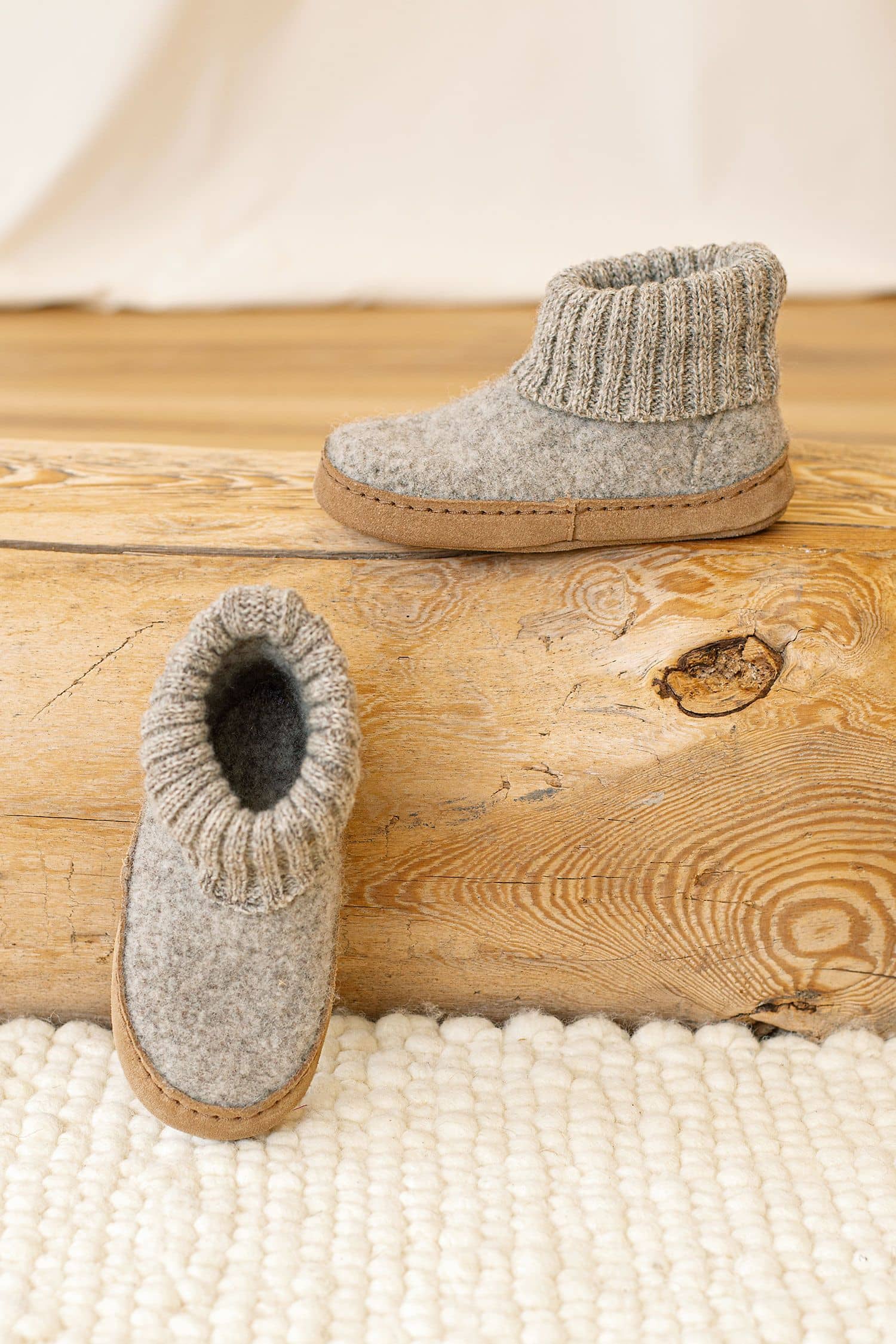 hellgraue Kinderhüttenschuhe vom Finkhof aus bio Wolle (kbT) und pflanzlich gegerbtem Leder stehen auf einem Holzstamm