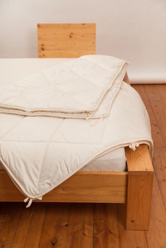 Kombi Steppdecke aus bio Wolle (kbT) und bio Baumwolle (kbA) vom Finkhof liegt auf braunem Holzbett