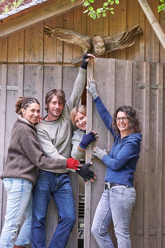Strickhandschuhe ohne Finger vier Models halten sich an Holztür von Schuppen mit farbigen fingerlosen Finkhof Strickhandschuhen aus bio Wolle (kbT)