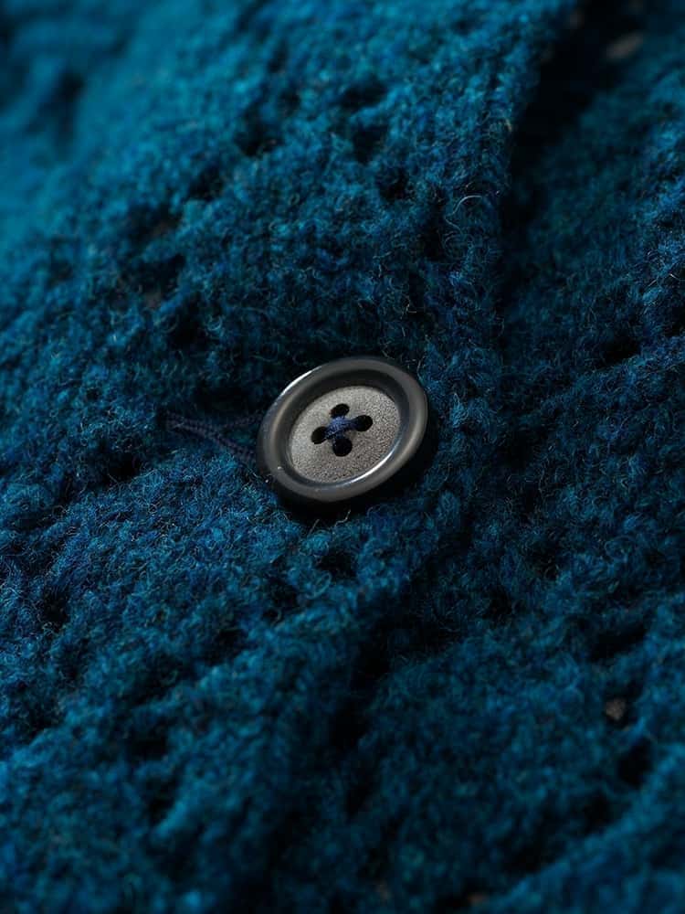 Nahaufnahme der Struktur und eines Knopfes der blauen Damenstrickjacke mit Ajourmuster aus Bio-Wolle vom Finkhof