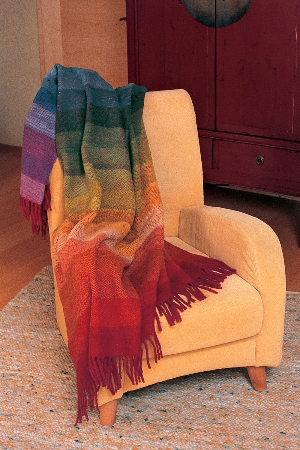 Finkhof Wolldecke Regenbogen aus bio Wolle (kbT) über orangen Sessel gelegt
