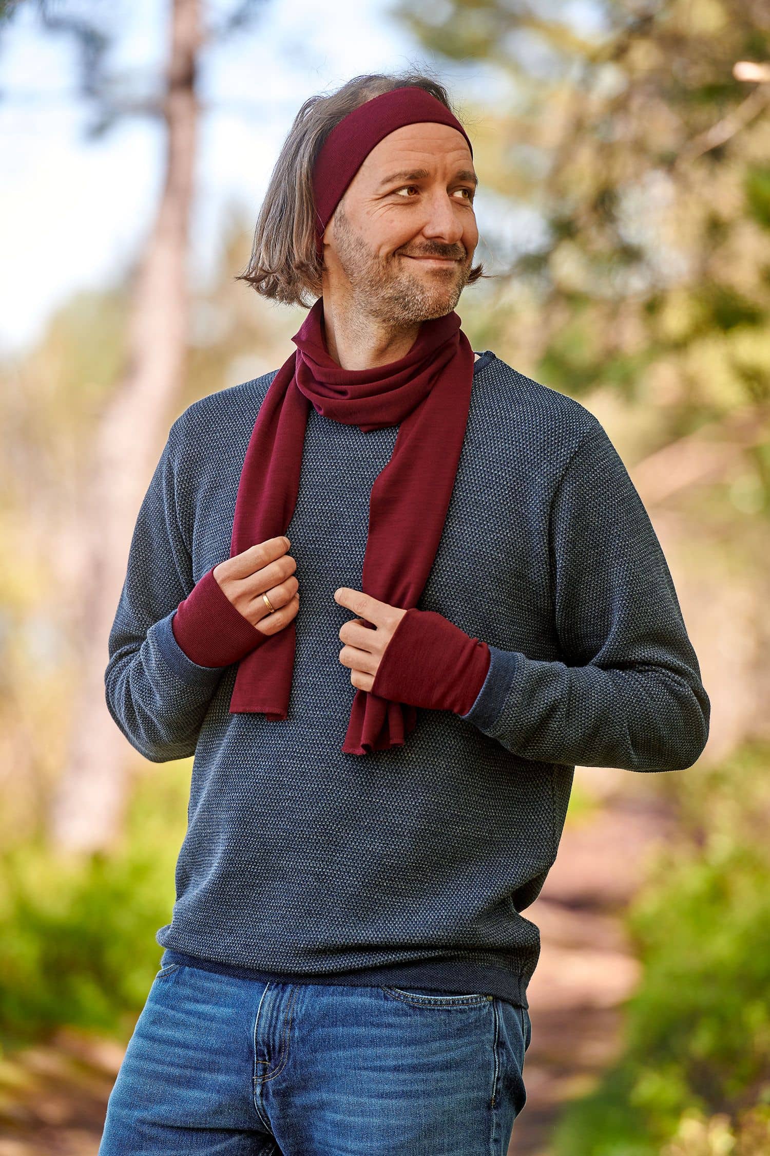 Mann mit blauem Pulli trägt bordeauxrote Pulswärmer aus bio Wolle (kbT) und Seide mit Schal und Stirnband