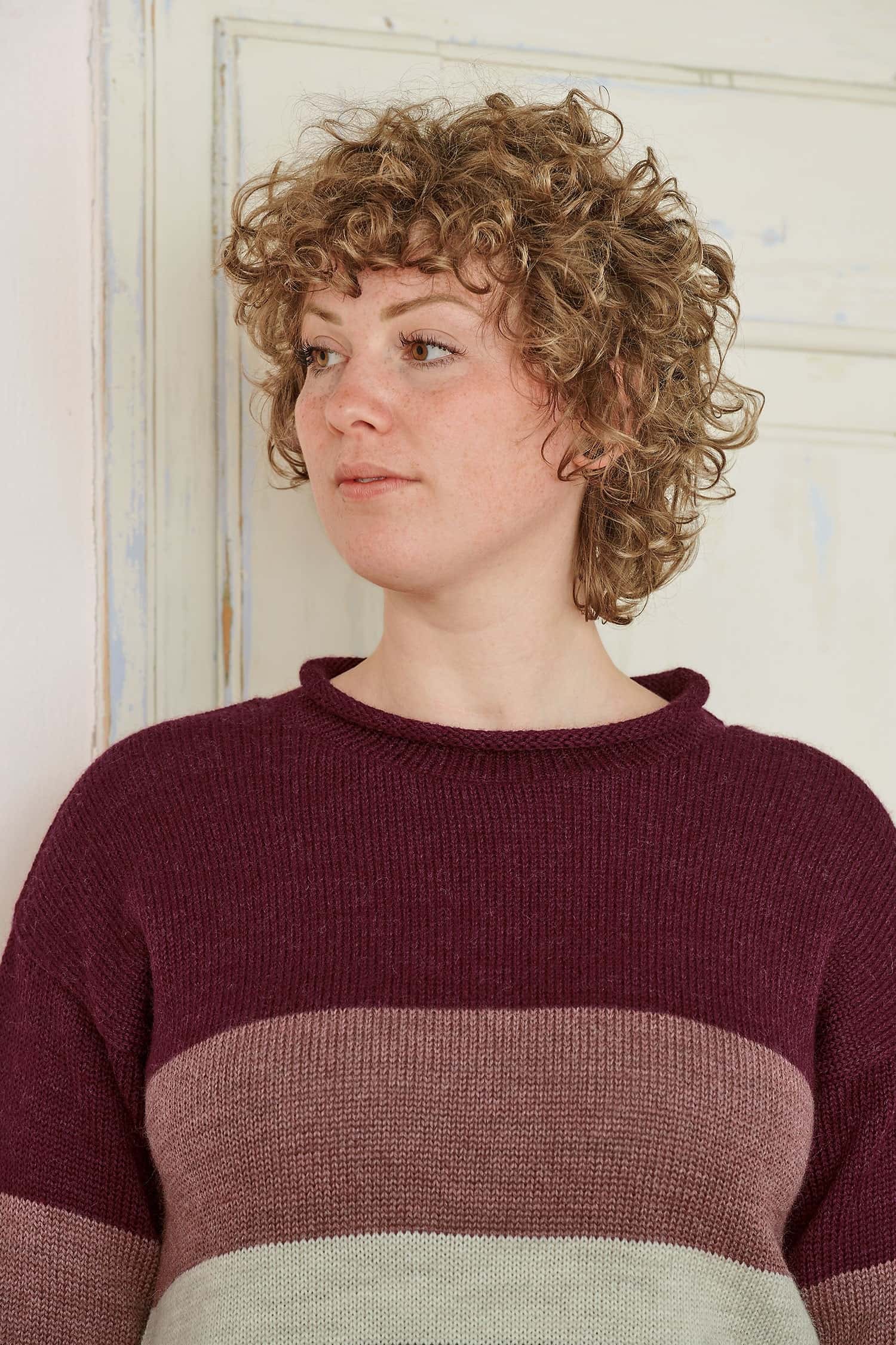 Frau mit blonden Locken trögt einen Pulli mit Blockstreifen in burgunderrot aus bio Wolle (kbT)