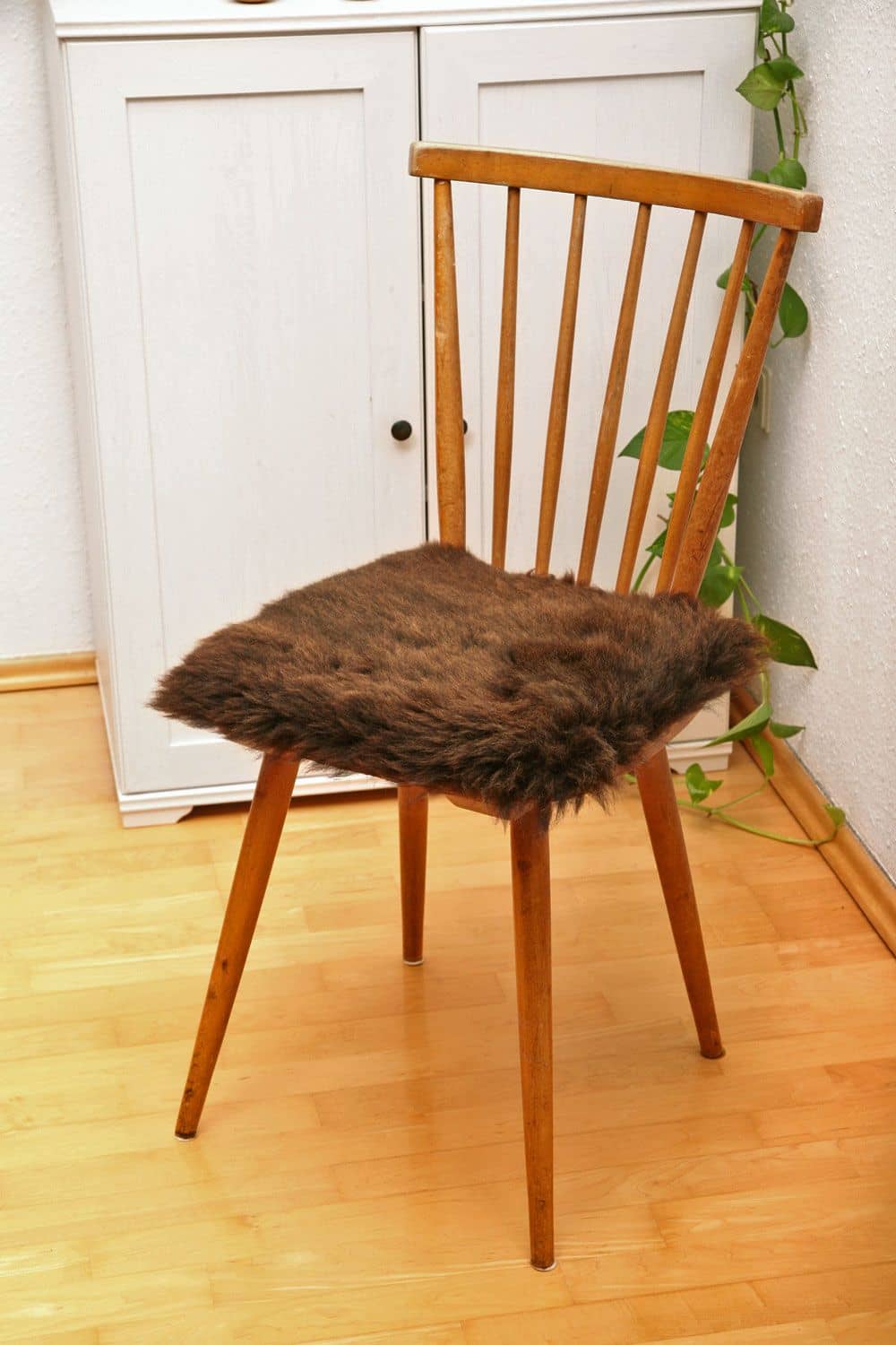 quadratische braune Stuhlauflage aus pflanzlich gegerbtem Schaffell auf braunem Holzstuhl