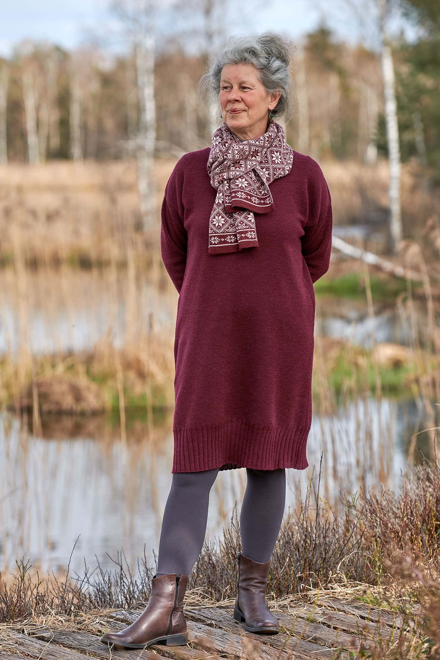 Frau trägt burgunderrotes Strickkleid aus bio Wolle (kbT), dazu einen rot gemusterten Schal