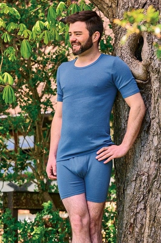 Mann lehnt an Baum und trägt ein blaues Kurzarmshirt aus bio Wolle (kbT) und eine kurze blaue Hose