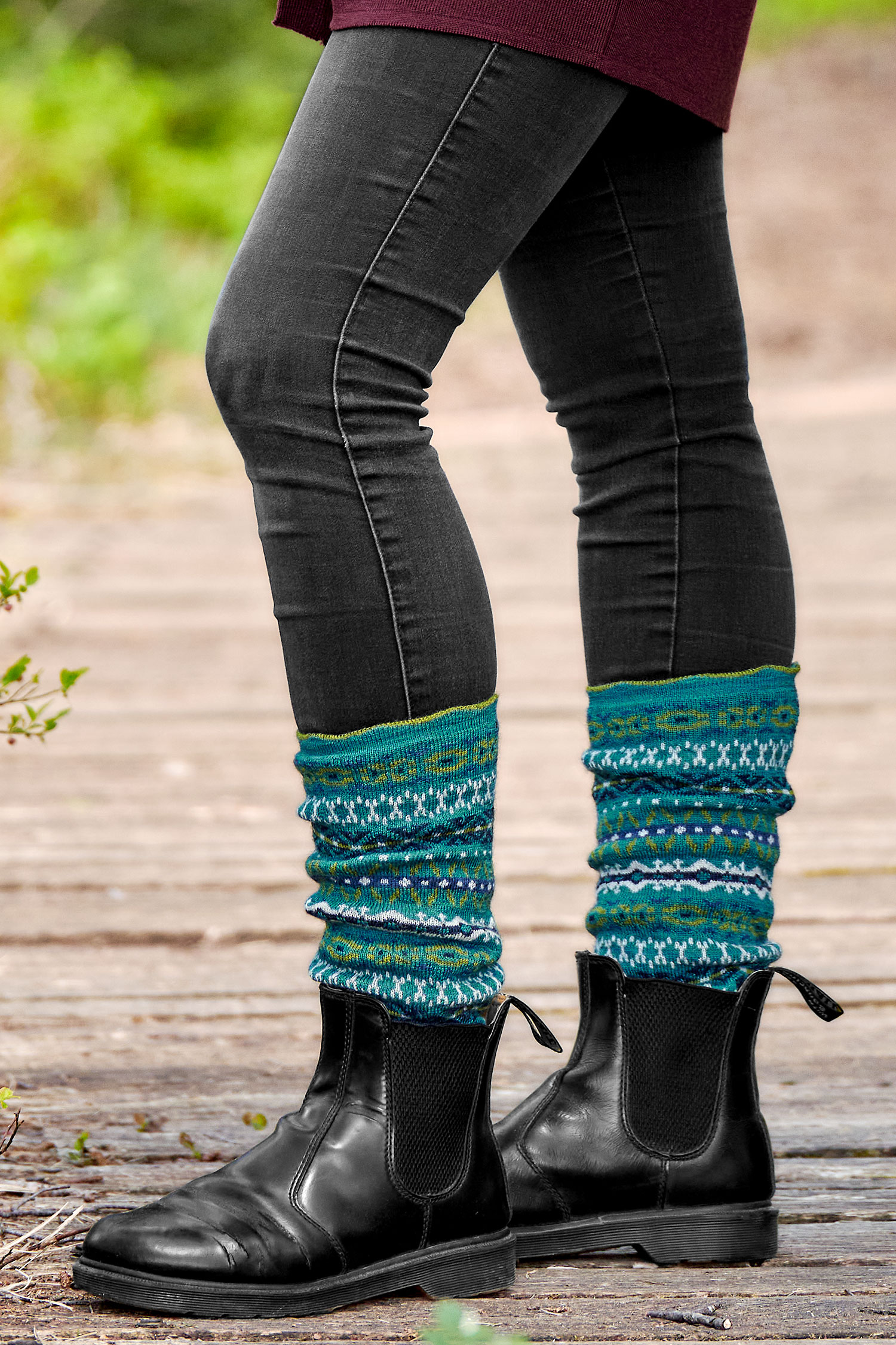 Person trägt schwarze Stiefel, Jeans und türkise Beinstulpen mit nordischem Muster aus bio Wolle (kbT)