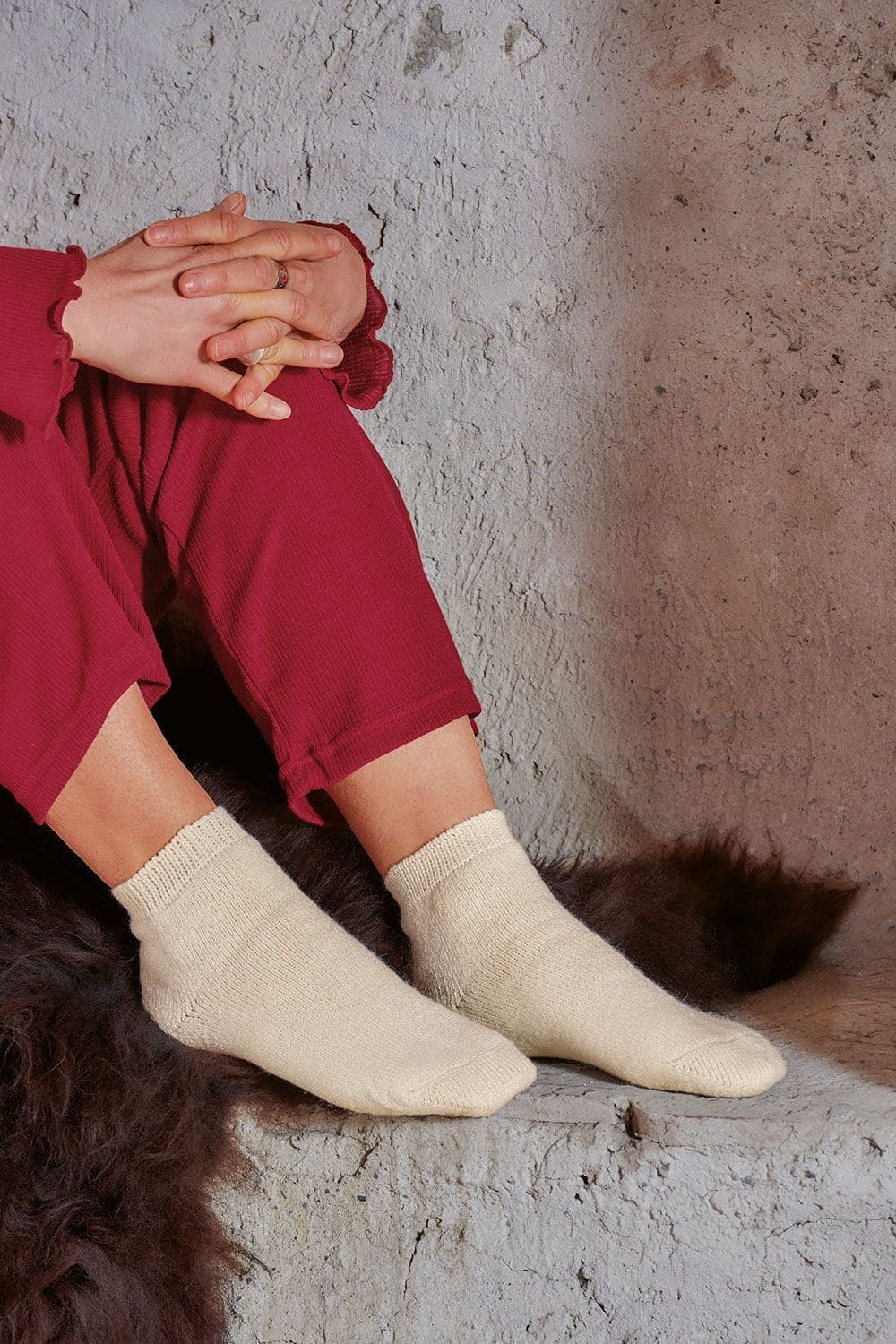 Bettsocken naturweiß Naturweiße Bettsocken aus Wolle und Seide getragen im Sitzen mit rotem Schlafanzug auf Felluntergrund