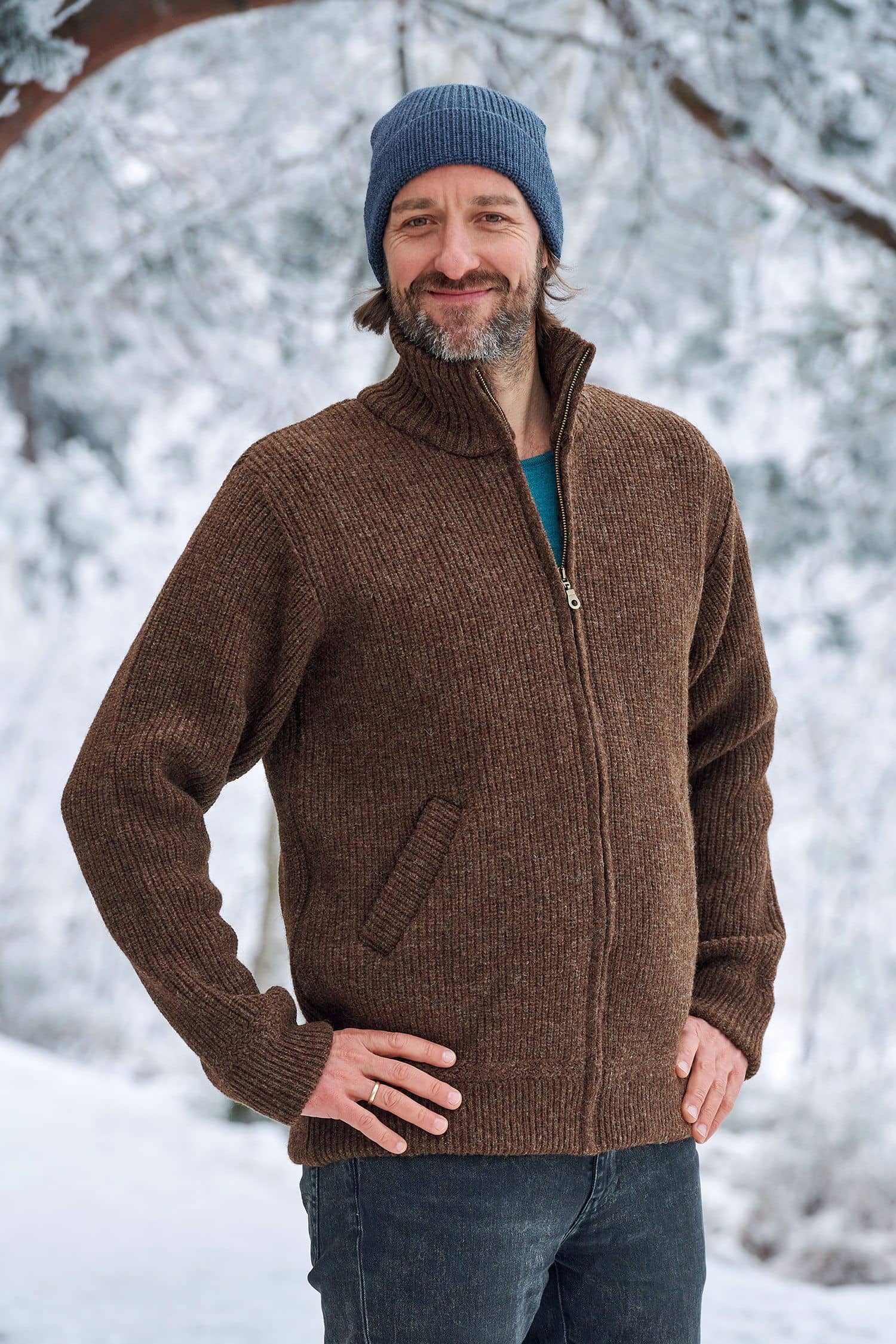 Mann in Schneelandschaft trägt eine braune Finkhof Jacke aus bio Wolle (kbT) und eine blaue Mütze