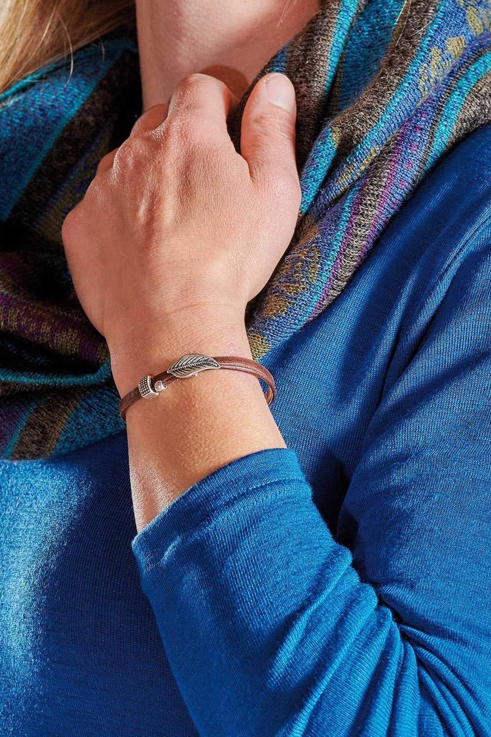 Person mit blauem Shirt trägt braunes Lederarmband mit silbernen Details aus pflanzlich gegerbtem Leder