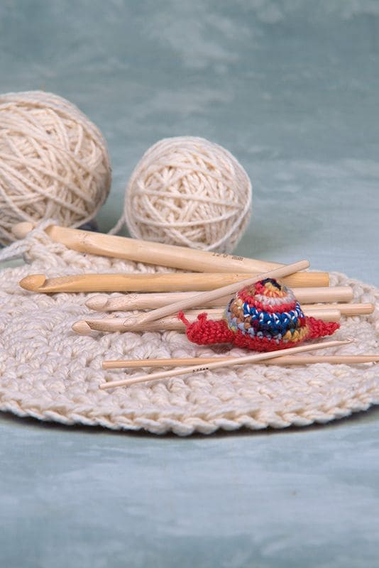 Häkelnadel aus Bambus Häkelnadeln aus Bambus liegen in verschiedenen Stärken auf beigem Strickstück mit Wollknäulen im Hintergrund