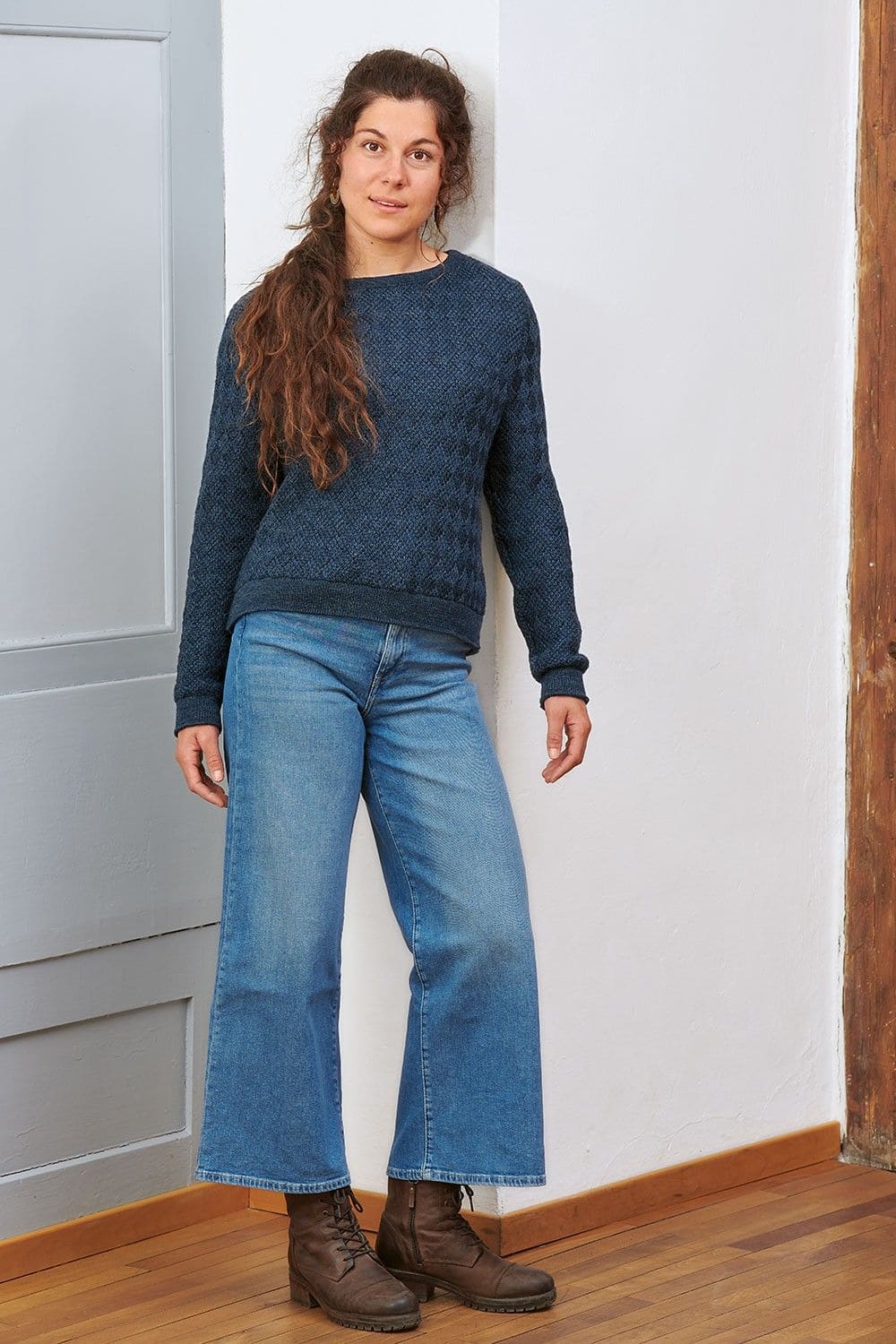 Frau lehnt sich mit nachtblauem Pullover aus bio Wolle (kbT) und blauer Jeans an Wand