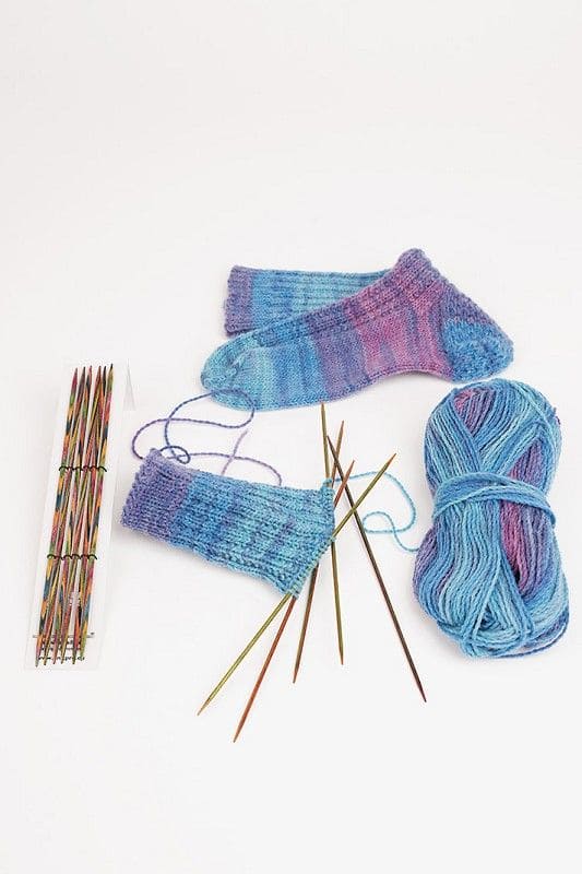 Nadelspiel bunt buntes Nadelspiel aus Birkenholz zusammen mit blau lila Stricksocken und Wolle auf weißem Untergrund